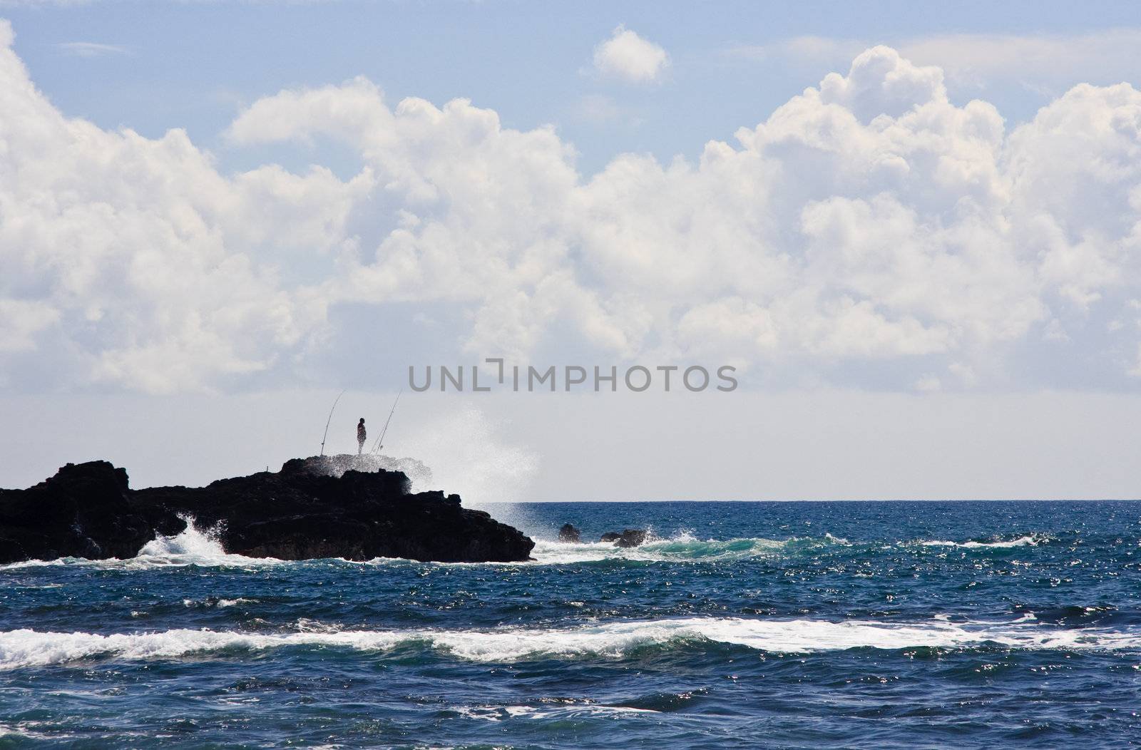Silhouette of a fisherman on rocky headland off the coast of Kauai