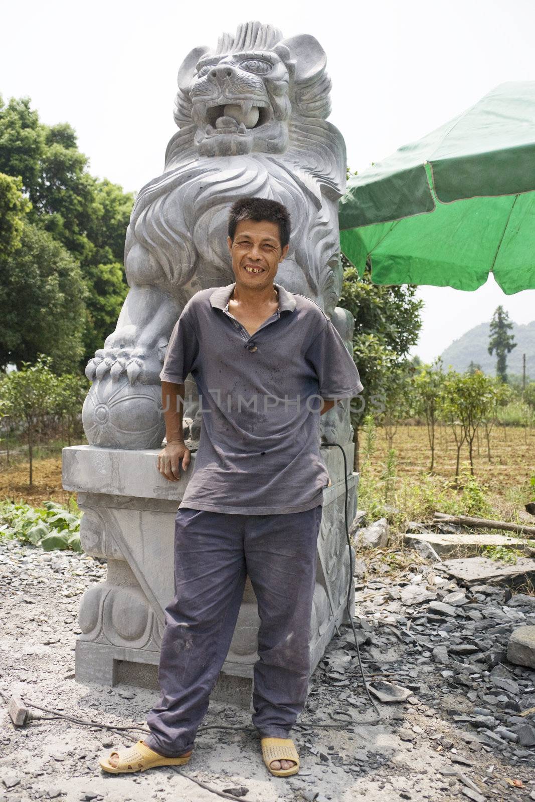 Image of a Chinese master craftsman beside his partially complete work of art of a stone lion at Guilin, China.