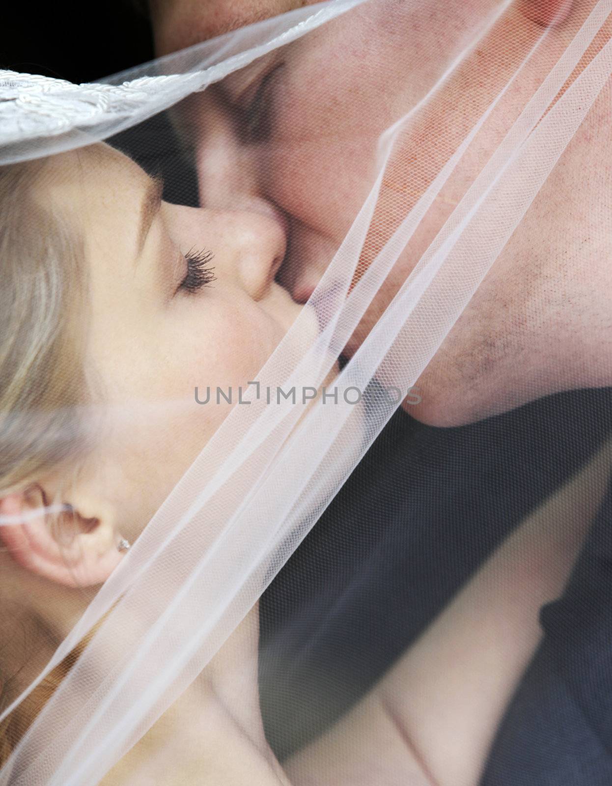 The groom and the bride kiss having closed by a veil