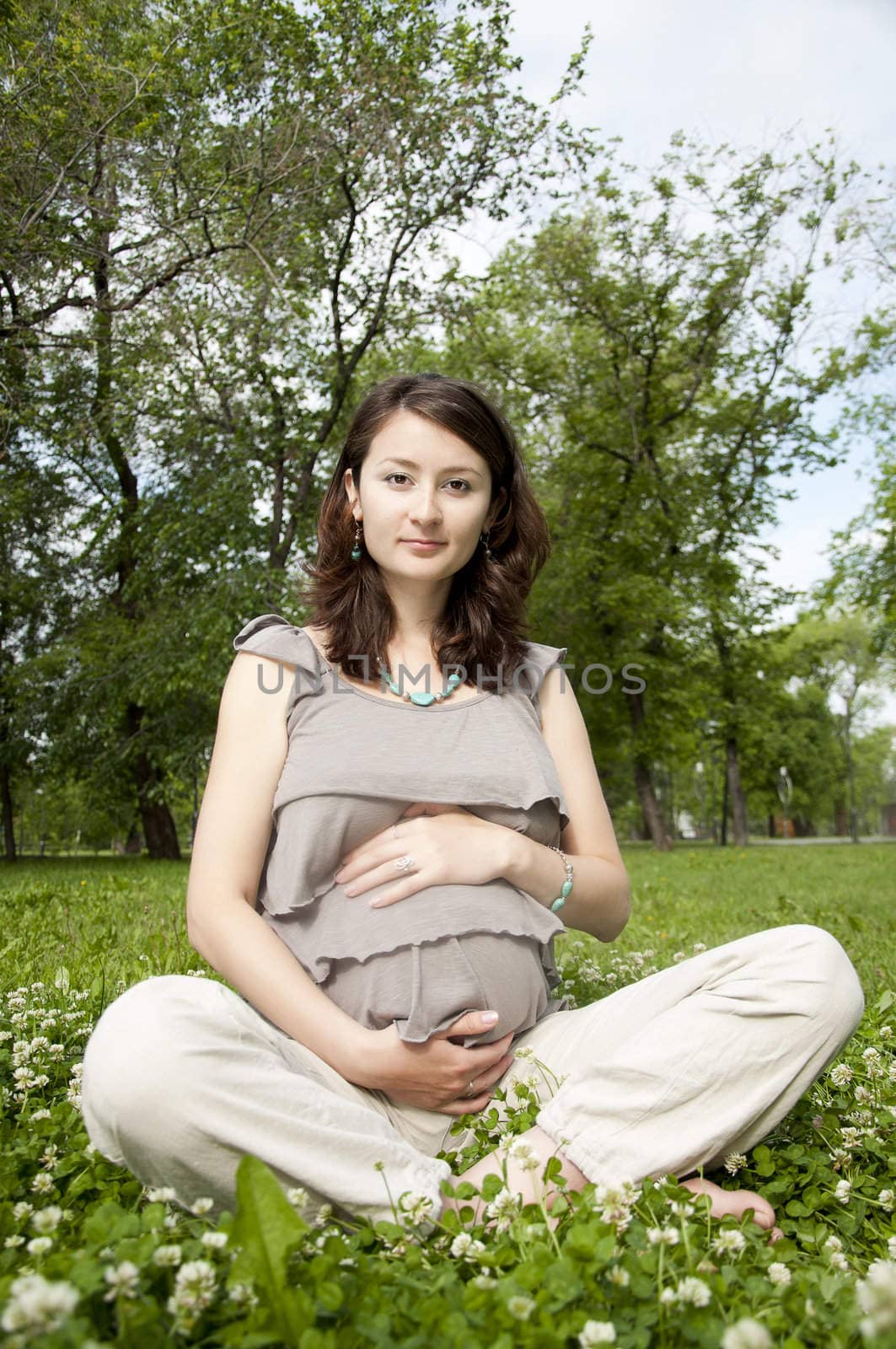 The portrait of the beautiful pregnant woman, sits on a grass