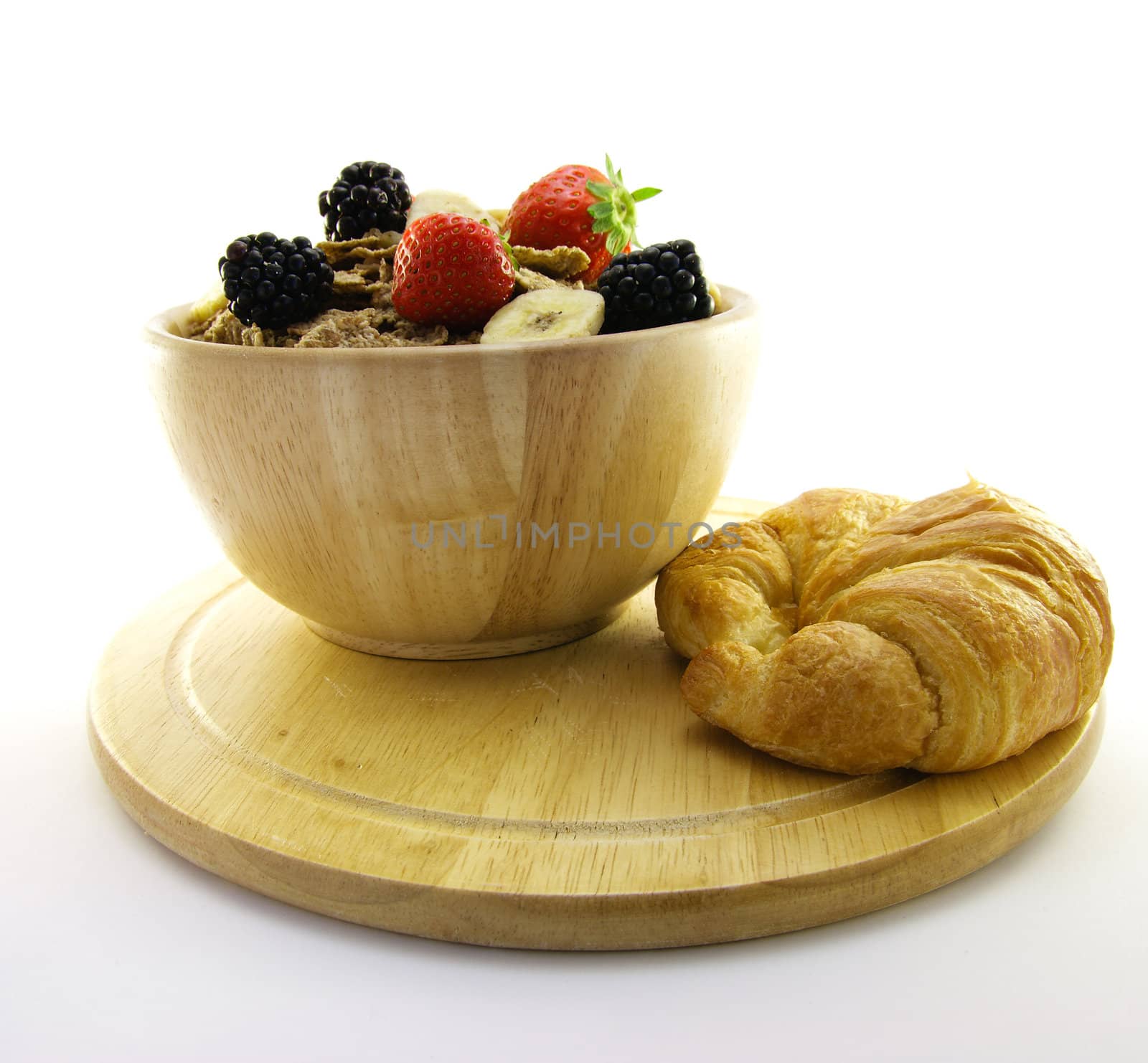 Crunchy looking delicious bran flakes and juicy fruit in a wooden bowl with a croissant on a white background