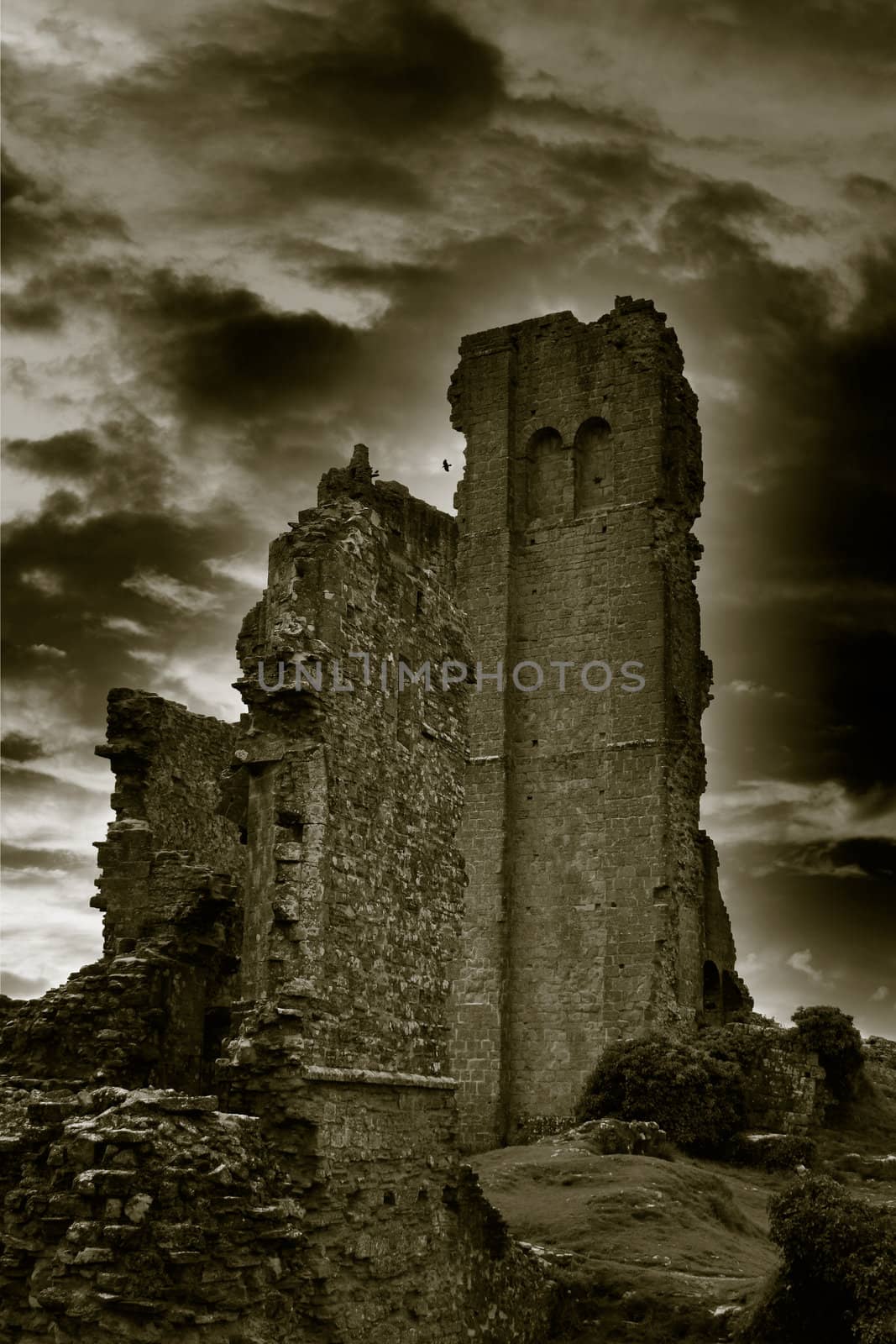 A mono image of Corfe Castle in Dorset with a dramatic cloud background and rolling fog at dusk.