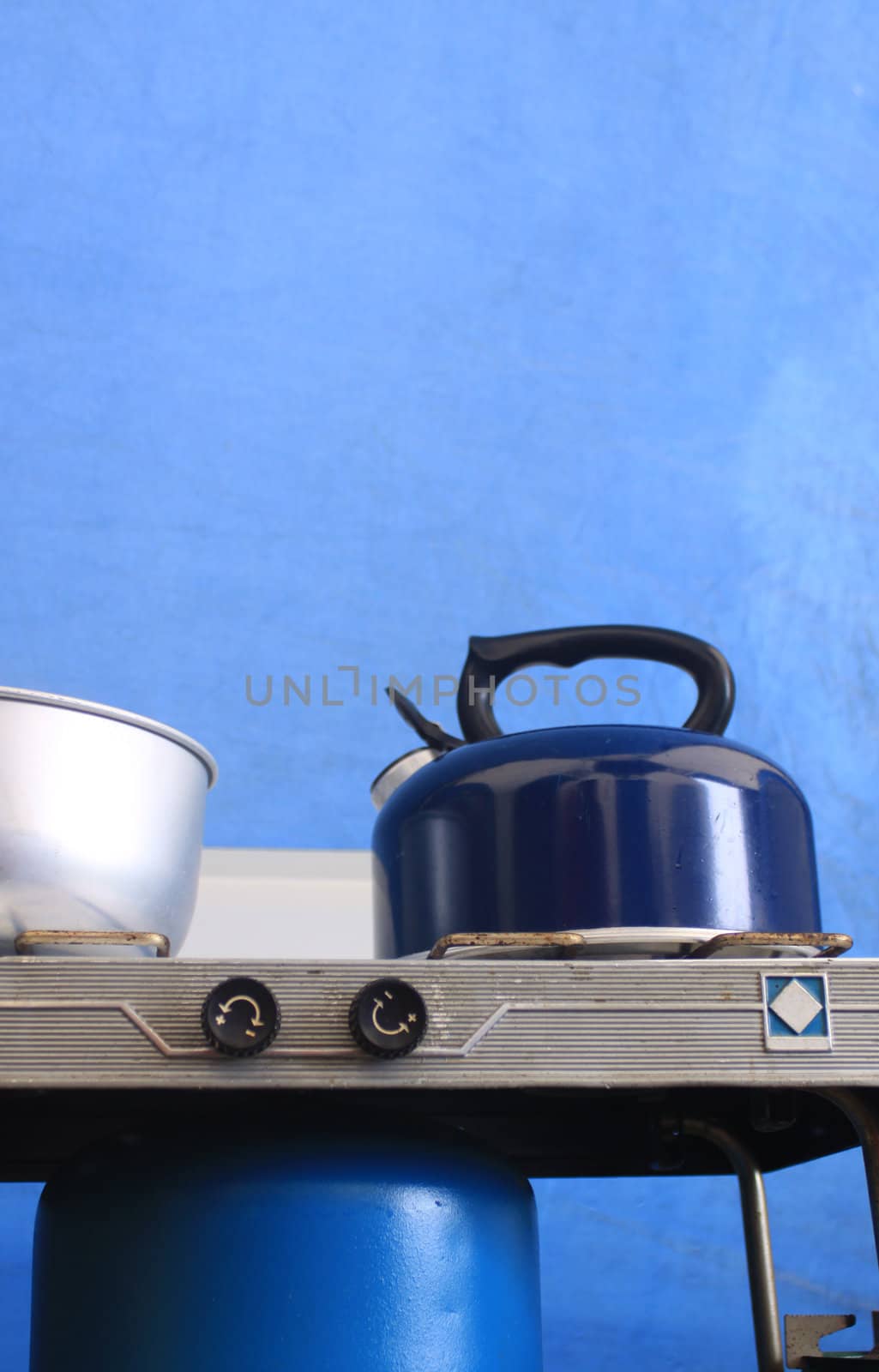 A blue kettle on top of a camping gas stove, set against a bue canvas tent background.