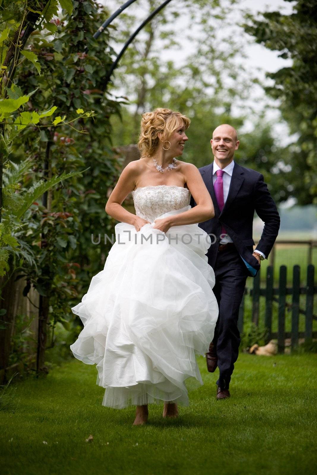 Beautiful bride running away from her new husband on barefeet through the grass
