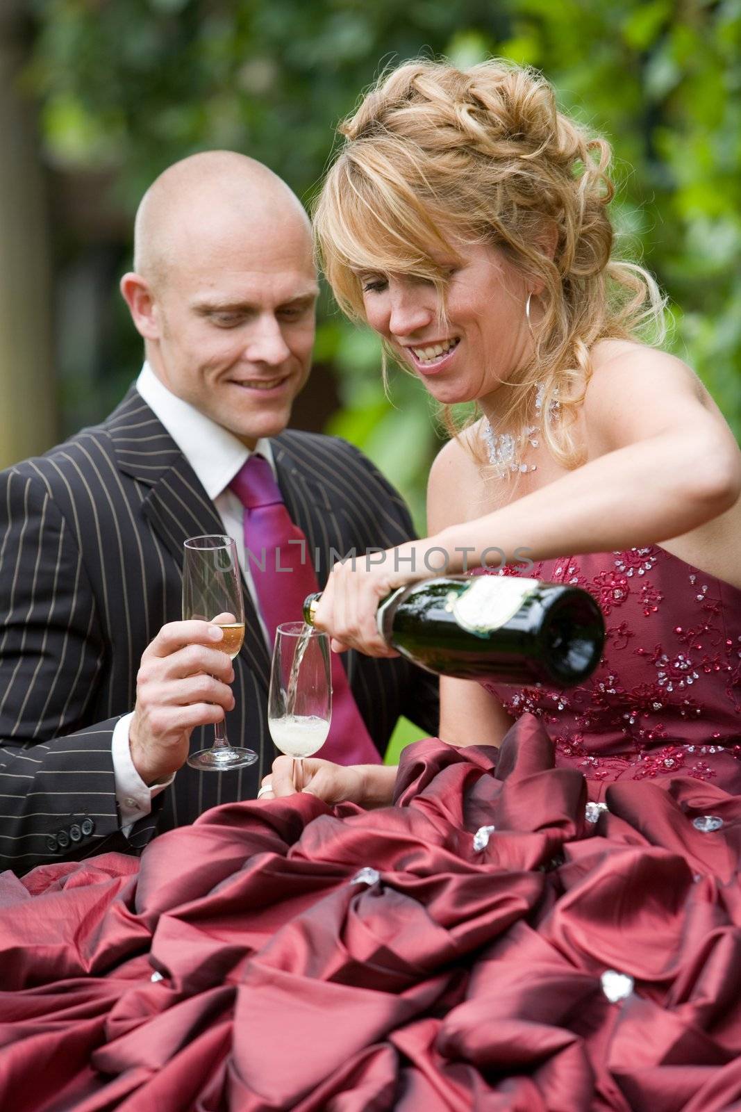 Beautiful newly wed couple having a drink outdoors with a bottle of champagne and glasses (shallow dof, focus on bride)