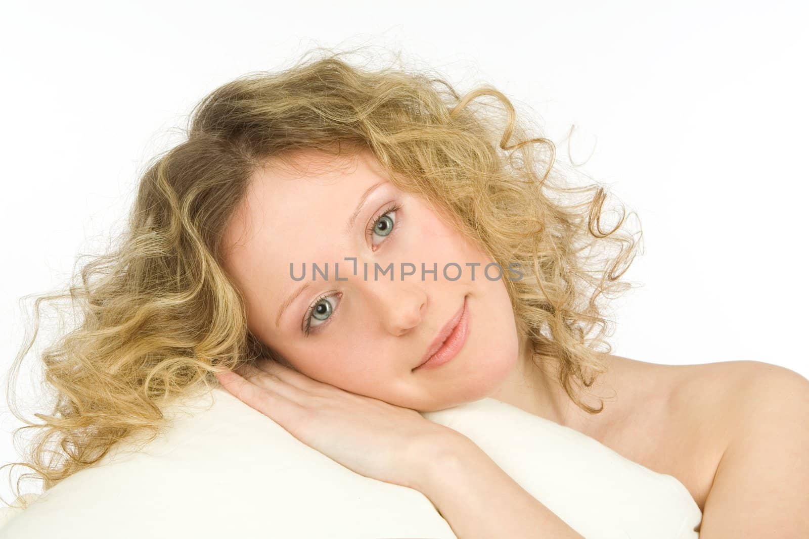 The young girl with open eyes and light hair lays on a white pillow on a white background 
