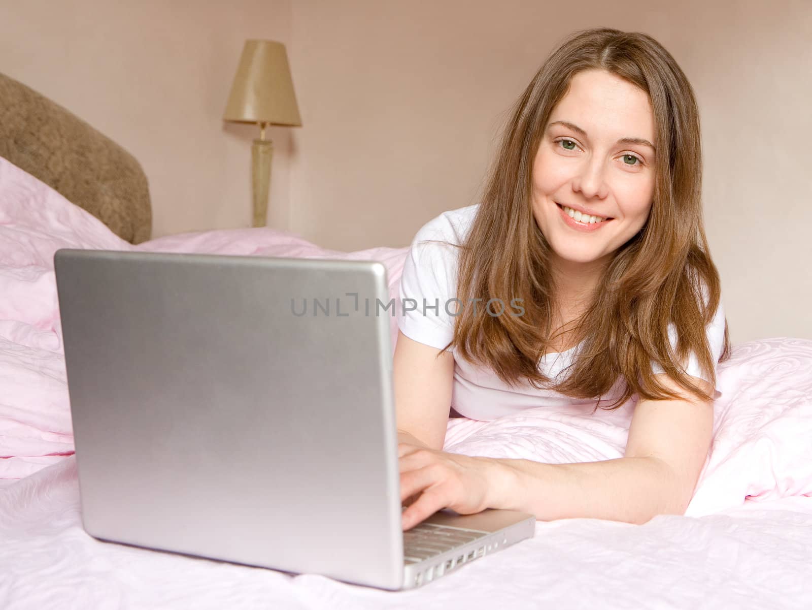 The young girl lays on bed with the computer
