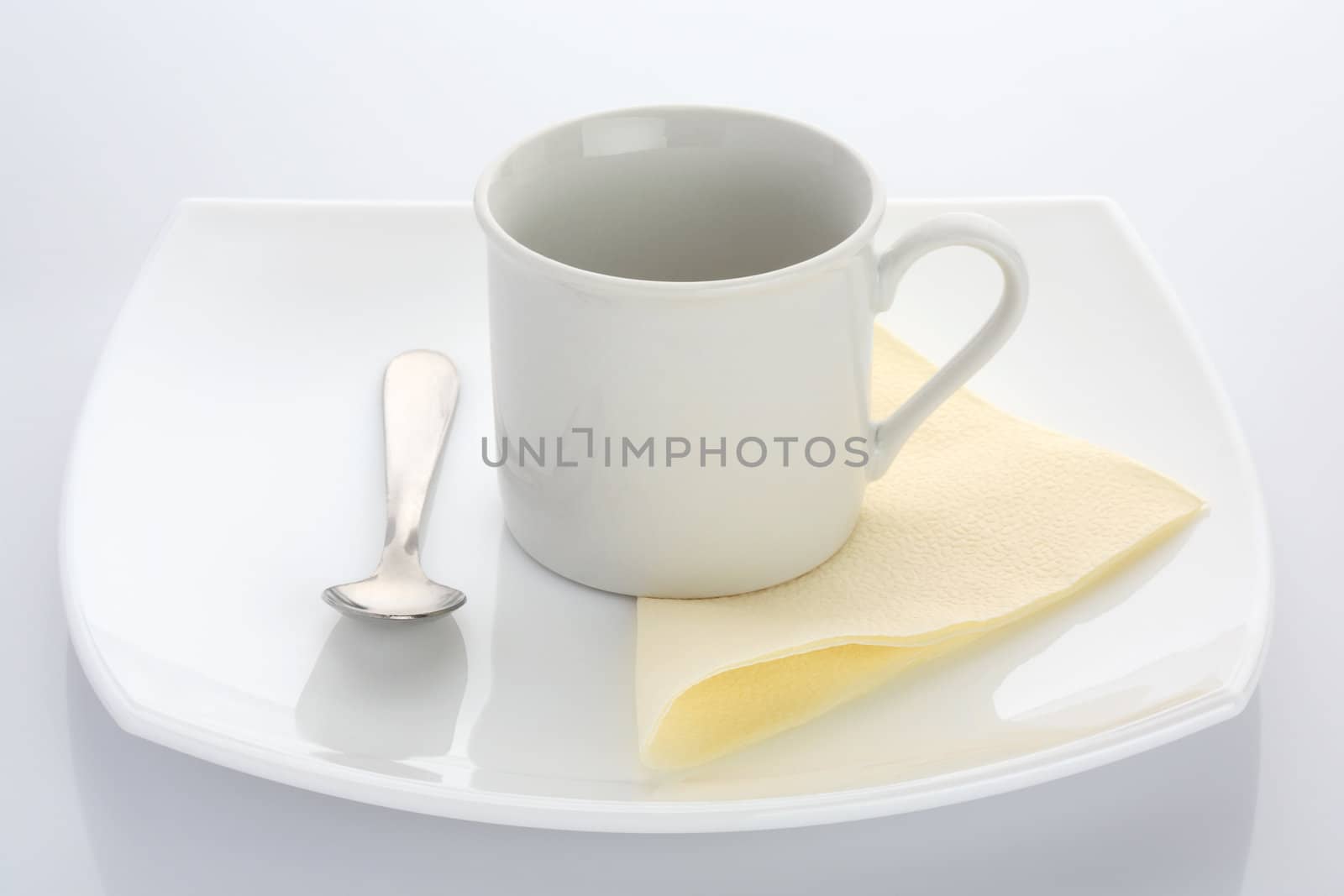 White cup with a yellow napkin and a spoon on a white plate
