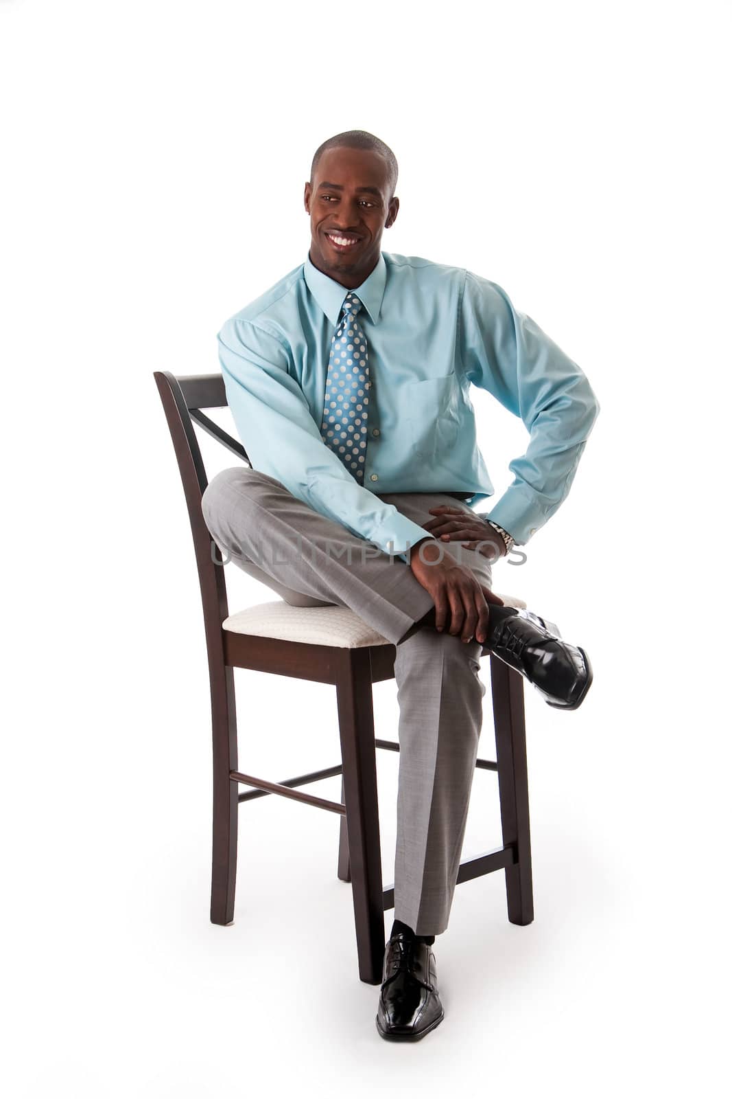 Handsome African American business man smiling sitting on chair, wearing sea green shirt and gray pants, isolated