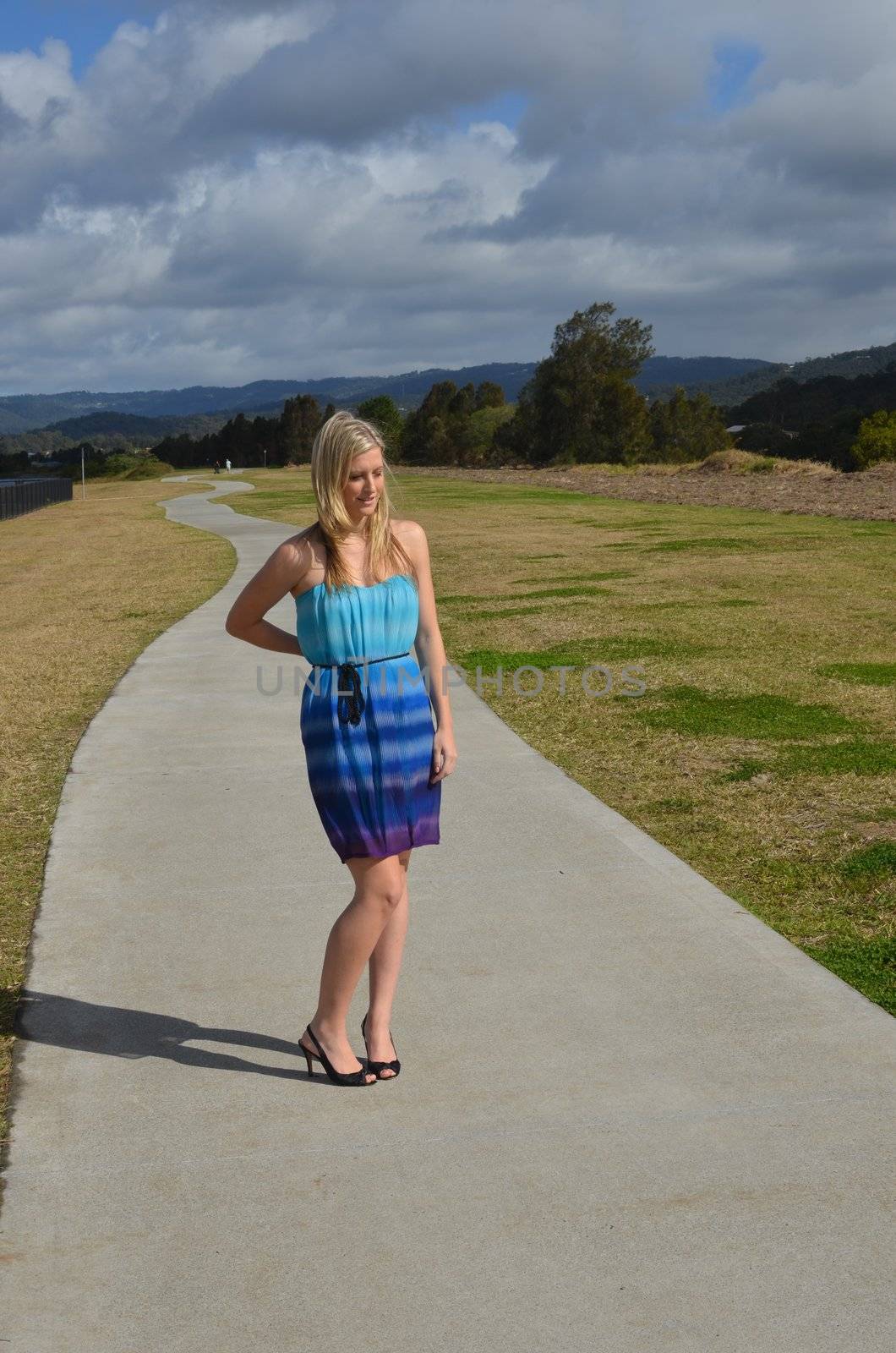 Blond lady in her cocktail dress standing on a long winding concrete path