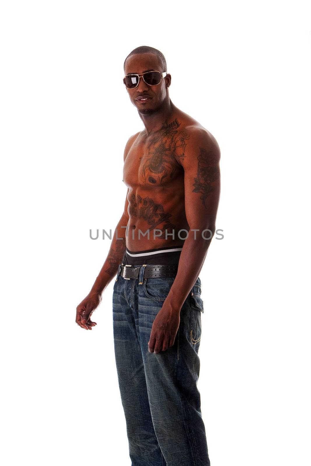 Handsome fit African American male with tough attitude standing sideways, toned body and tattoos, wearing blue jeans and sunglasses, showing rim of underwear, isolated