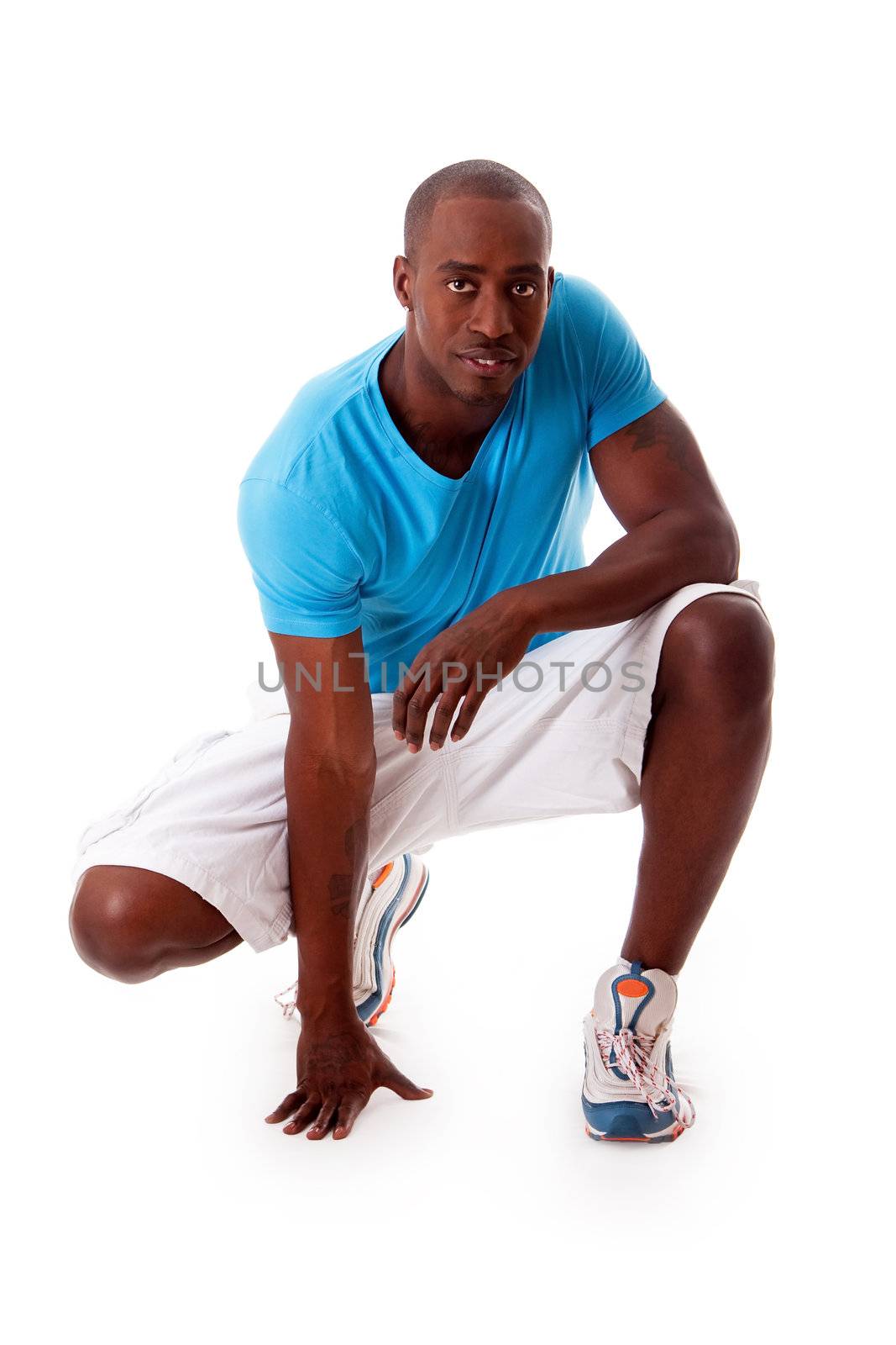 Handsome African American sporty man crouching wearing blue shirt, isolated