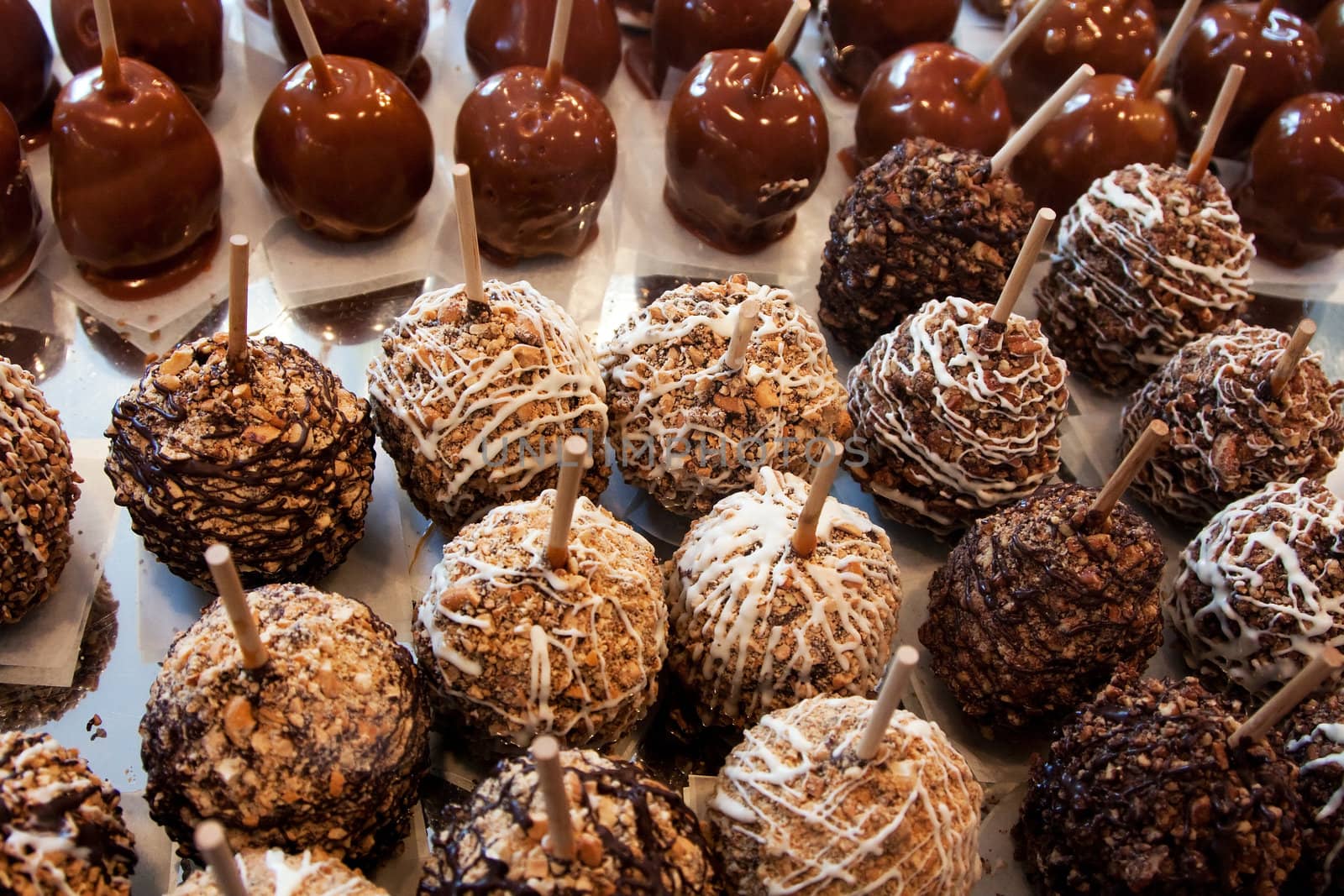 Variety of delicious candy apples covered with white, milk and dark chocolate, caramel and nuts on a stick on display