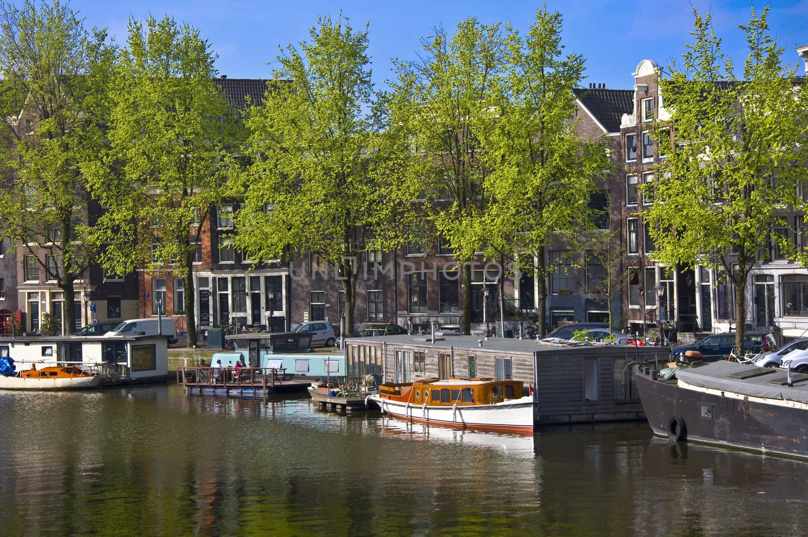 Classic view of Amsterdam. Embankment with barge. Green trees against the background of Dutch houses.