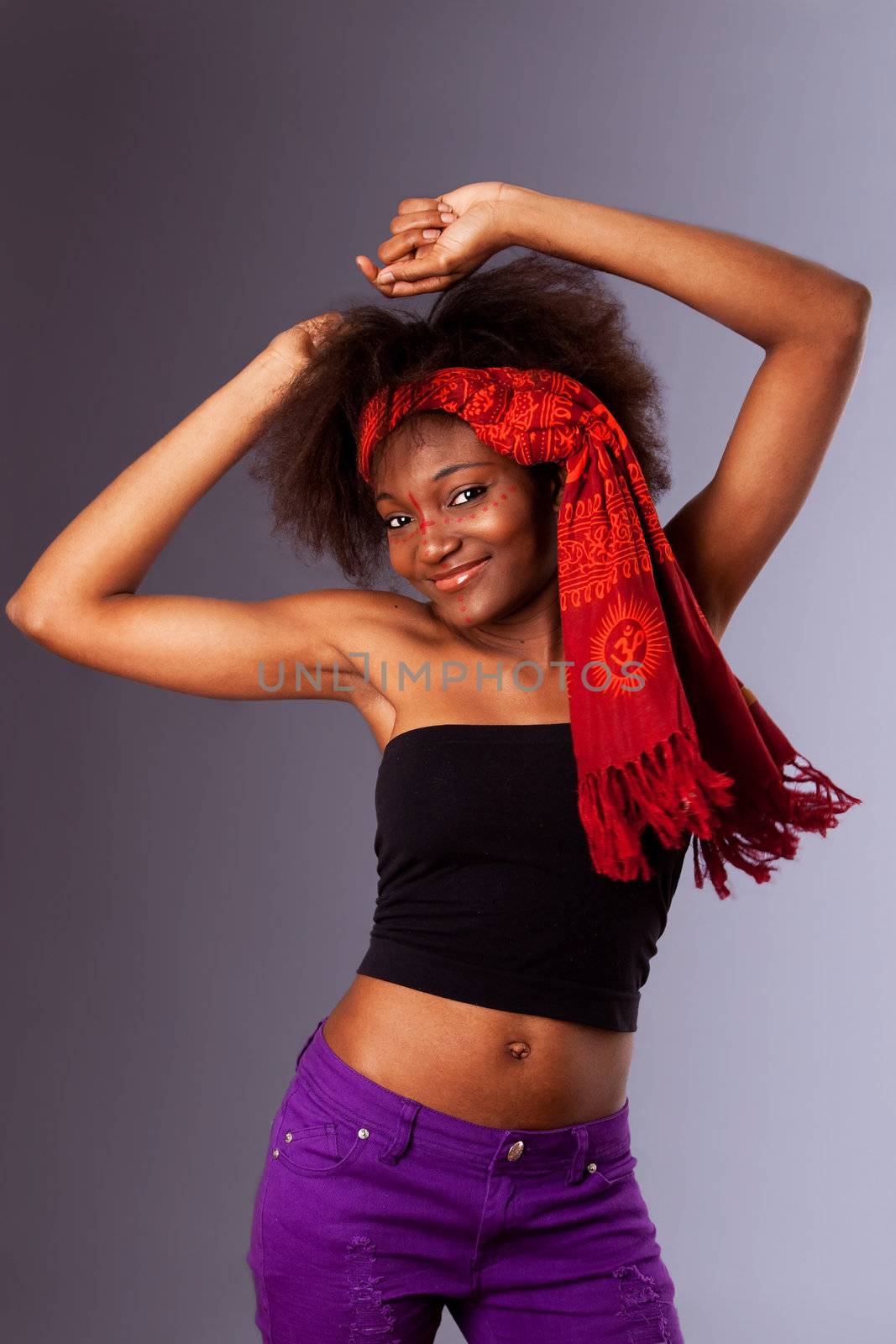 Beautiful young African-American girl happy and smiling and partying, dressed in a black tube top, purple pants and red head scarf heaving frizzy afro hair, dancing with arm above her head, isolated