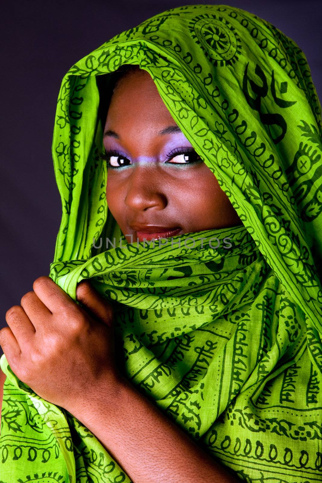 The face of an shy innocent beautiful young African-American woman covering her mouth with green headwrap and purple-green makeup, isolated