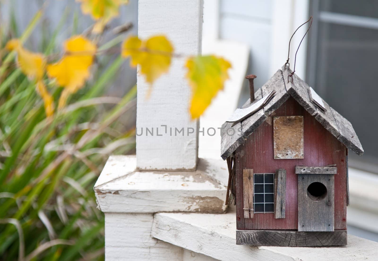 Country folk style bird house on front porch railing