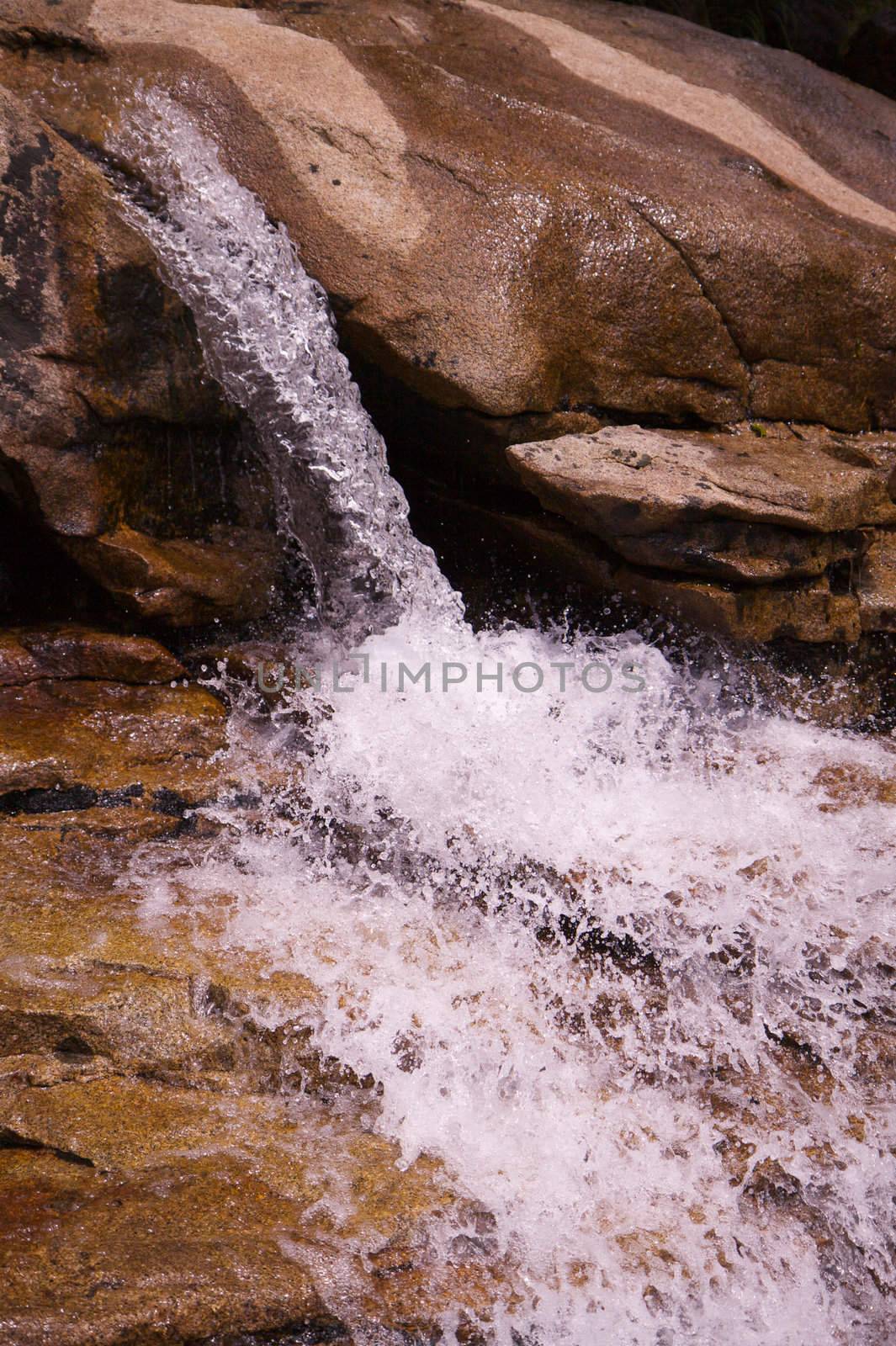 Small single waterfall cascading down mountain boulders into cascading water in HDR high dynamic range