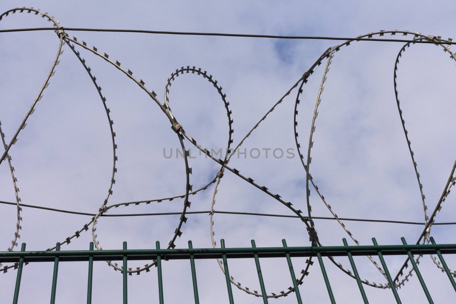 High-security fence with razor wire crown before partly clouded blue sky.