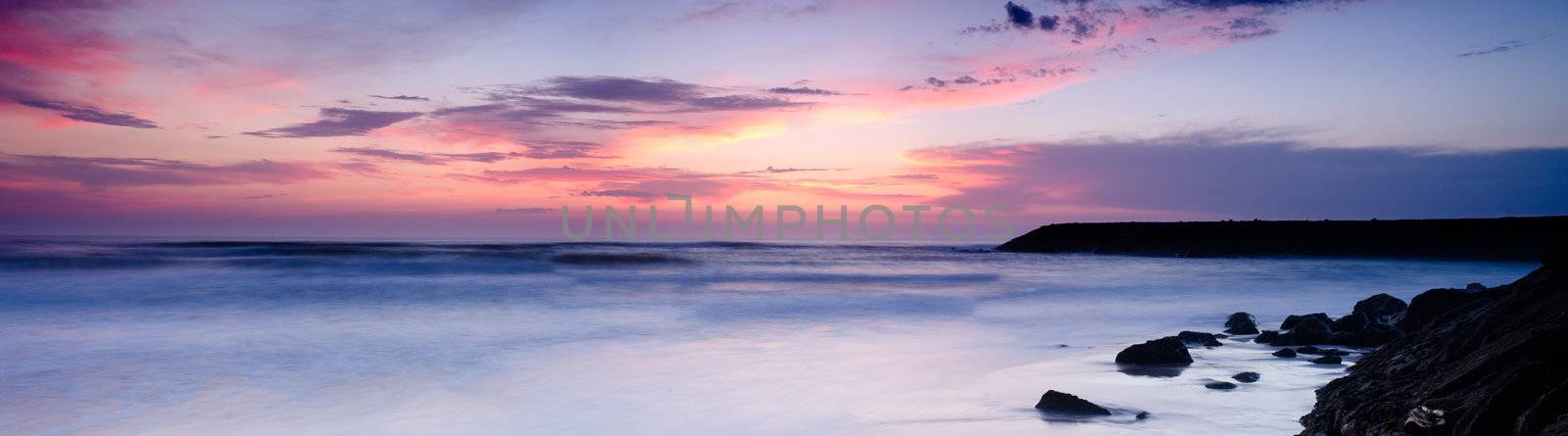Sunset on a beach, beautiful sky and silky water arround rocks.