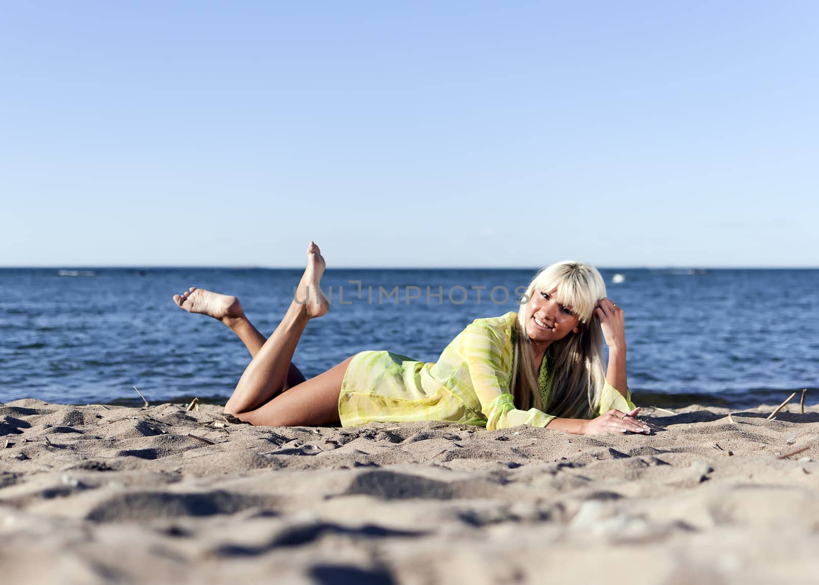 blonde girl in a yellow tunic lies near the sea on his knees by dmitrimaruta