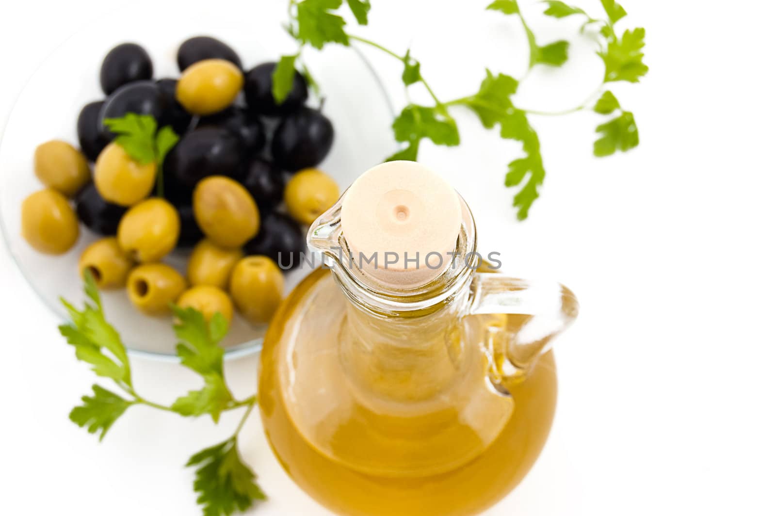 Olives and oil jug with greens on white, focus on cork