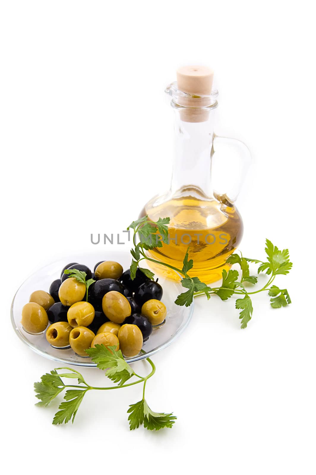 Olives and oil jug with greens on white, focus on olives