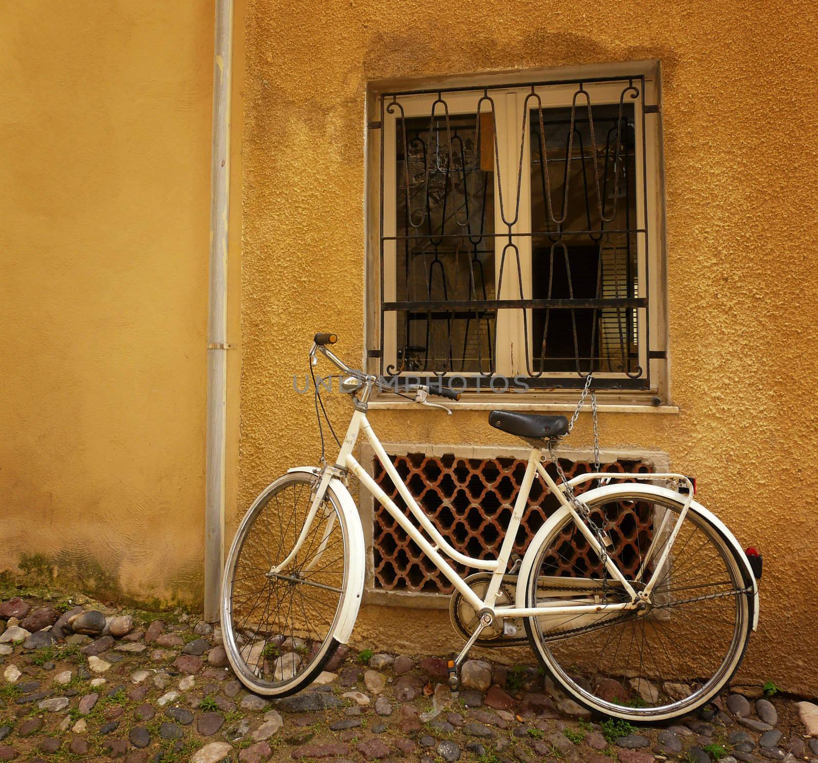 Old bicycle standing against a wall under a window.