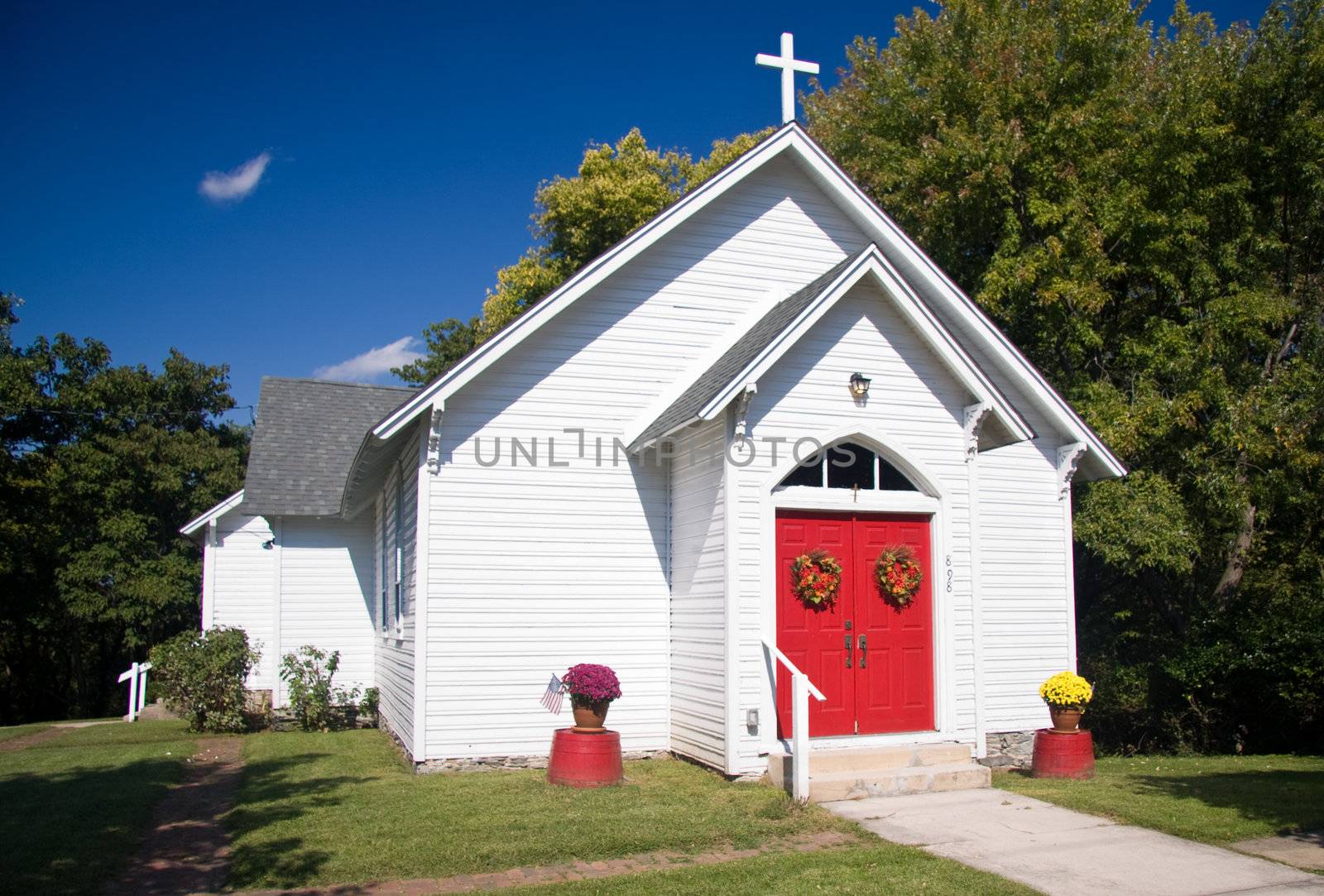 Bright white chapel with red doors decorated with fall flowers