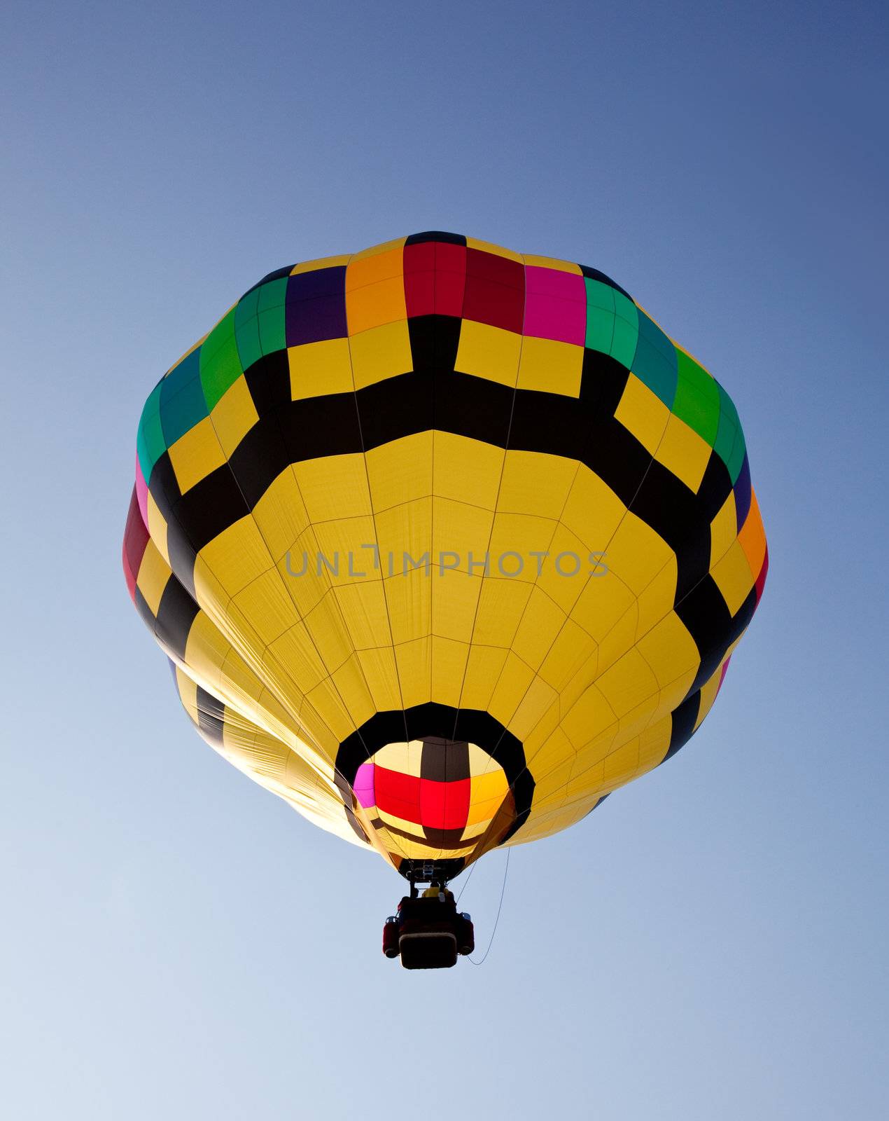 Yellow hot air balloon soaring skyward towards the sun