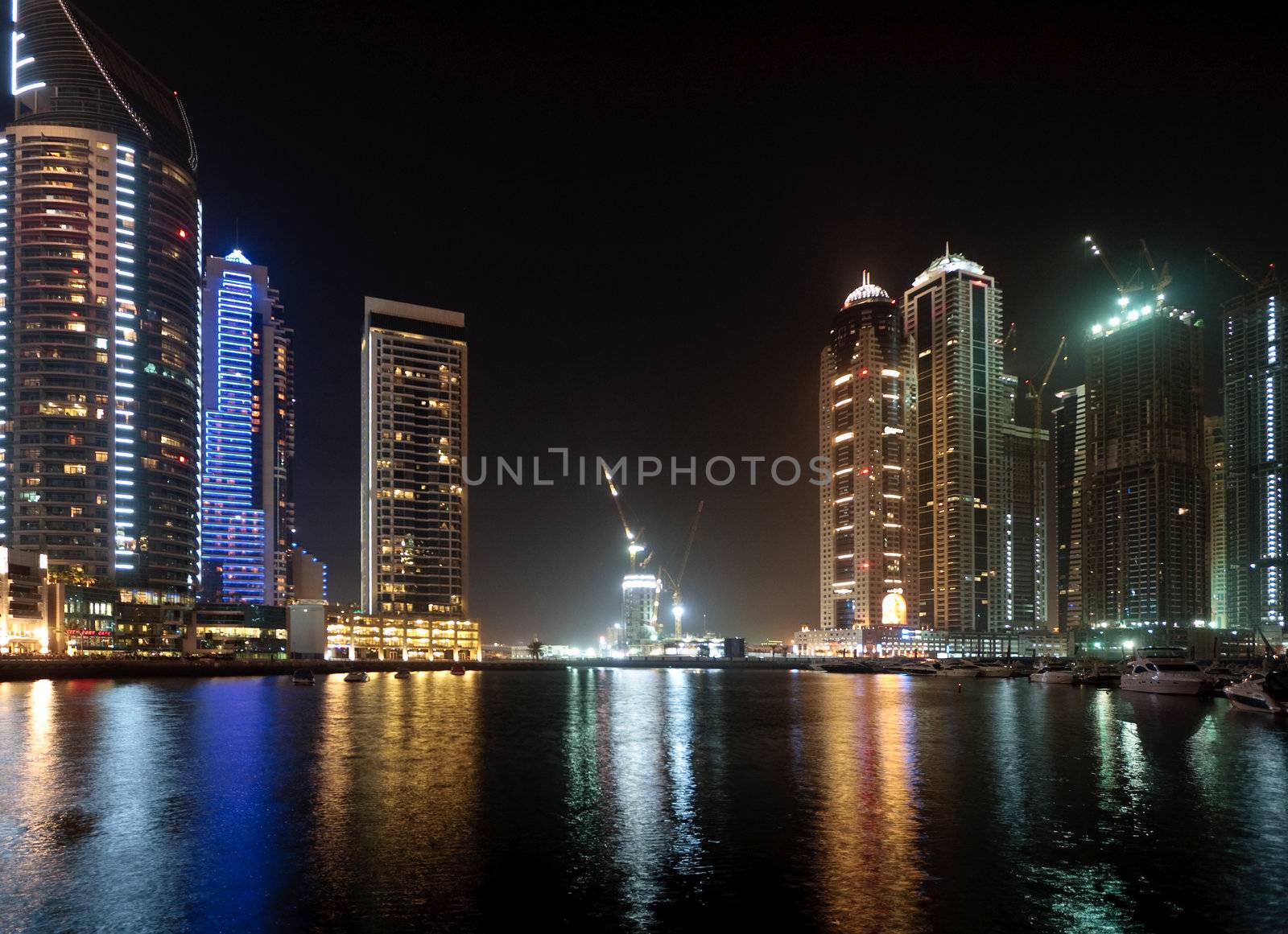 Modern skyscrapers reflected in the marina in Dubai with a contruction underway in the center