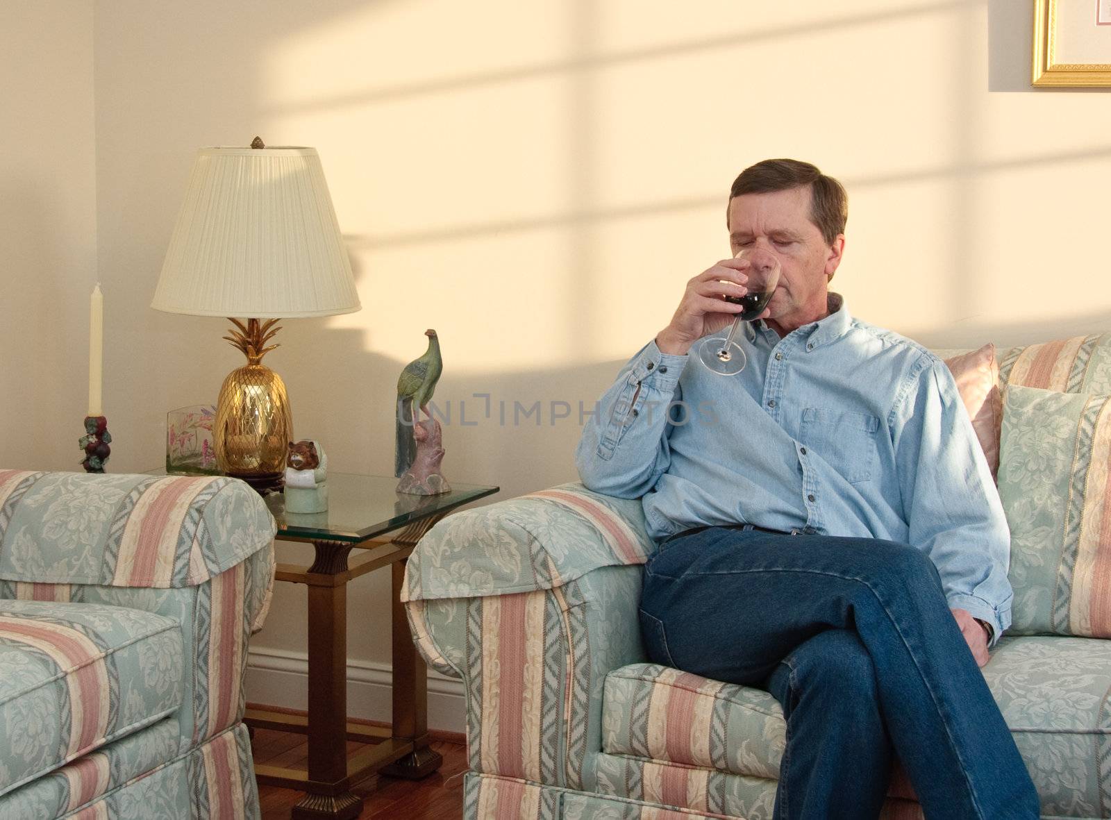 Middle-aged man relaxes on sofa in modern living room drinking a glass of red wine