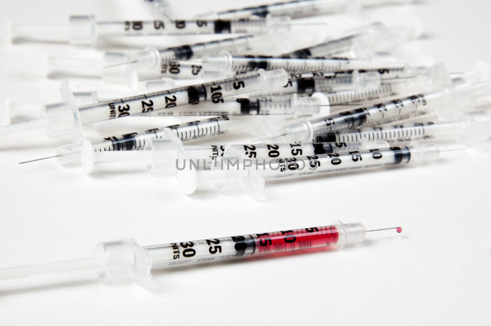 Pile of used syringes with a single filled one by steheap
