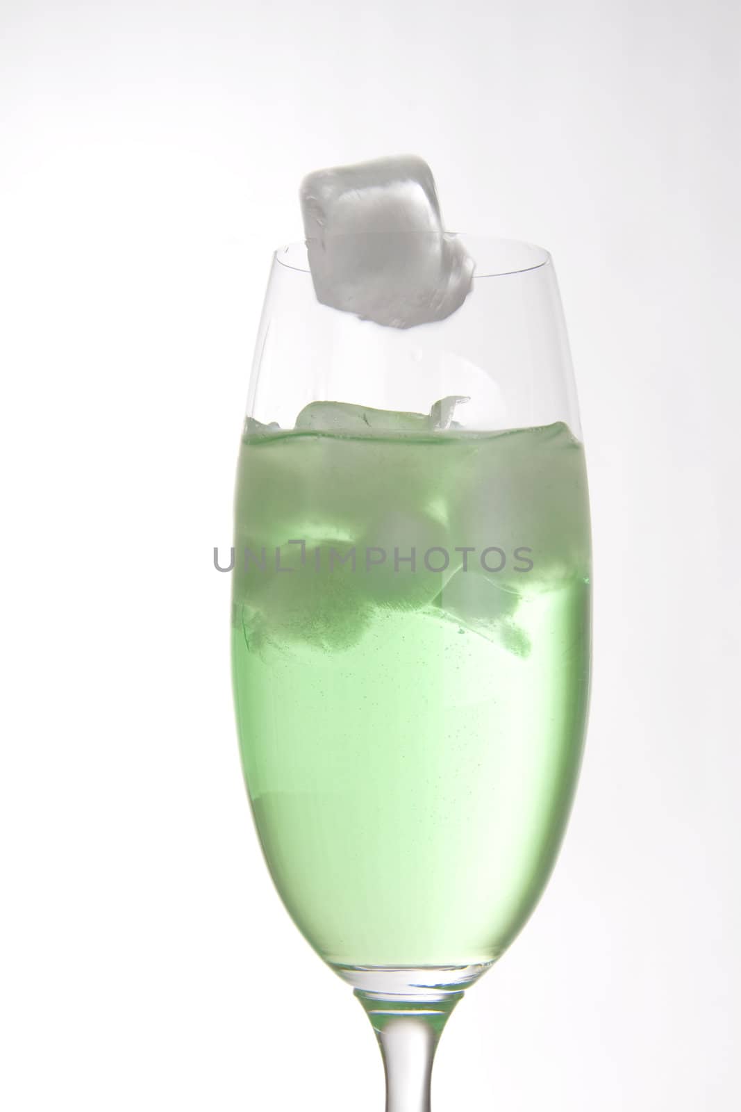 Ice cube falling into a bright green drink in a tall champagne glass