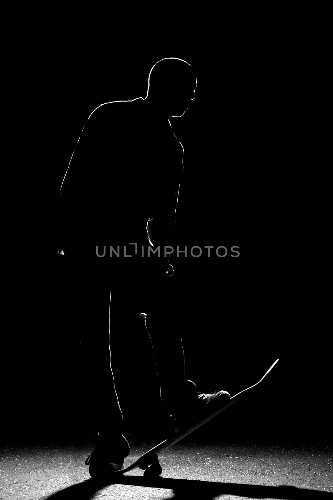 A backlit skateboarder guy posing under dramatic rim lighting with his skateboard flipped up in the front.