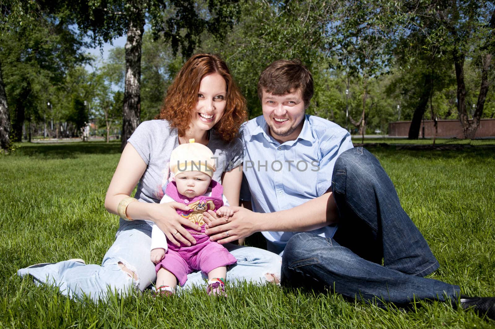 The young family in park, sits on a grass and smiles