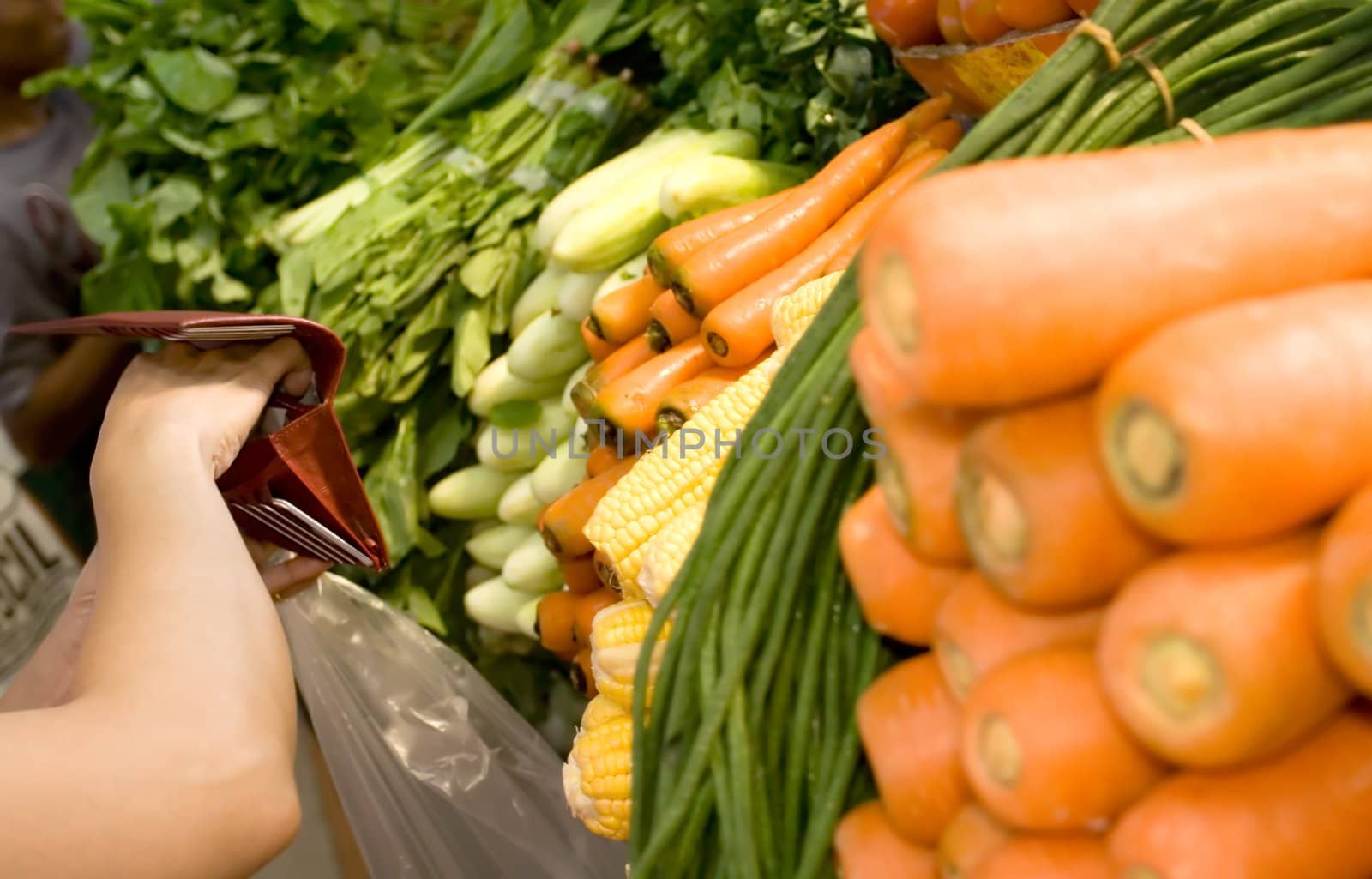 woman opening her wallet to pay for purchased vegetables at the market