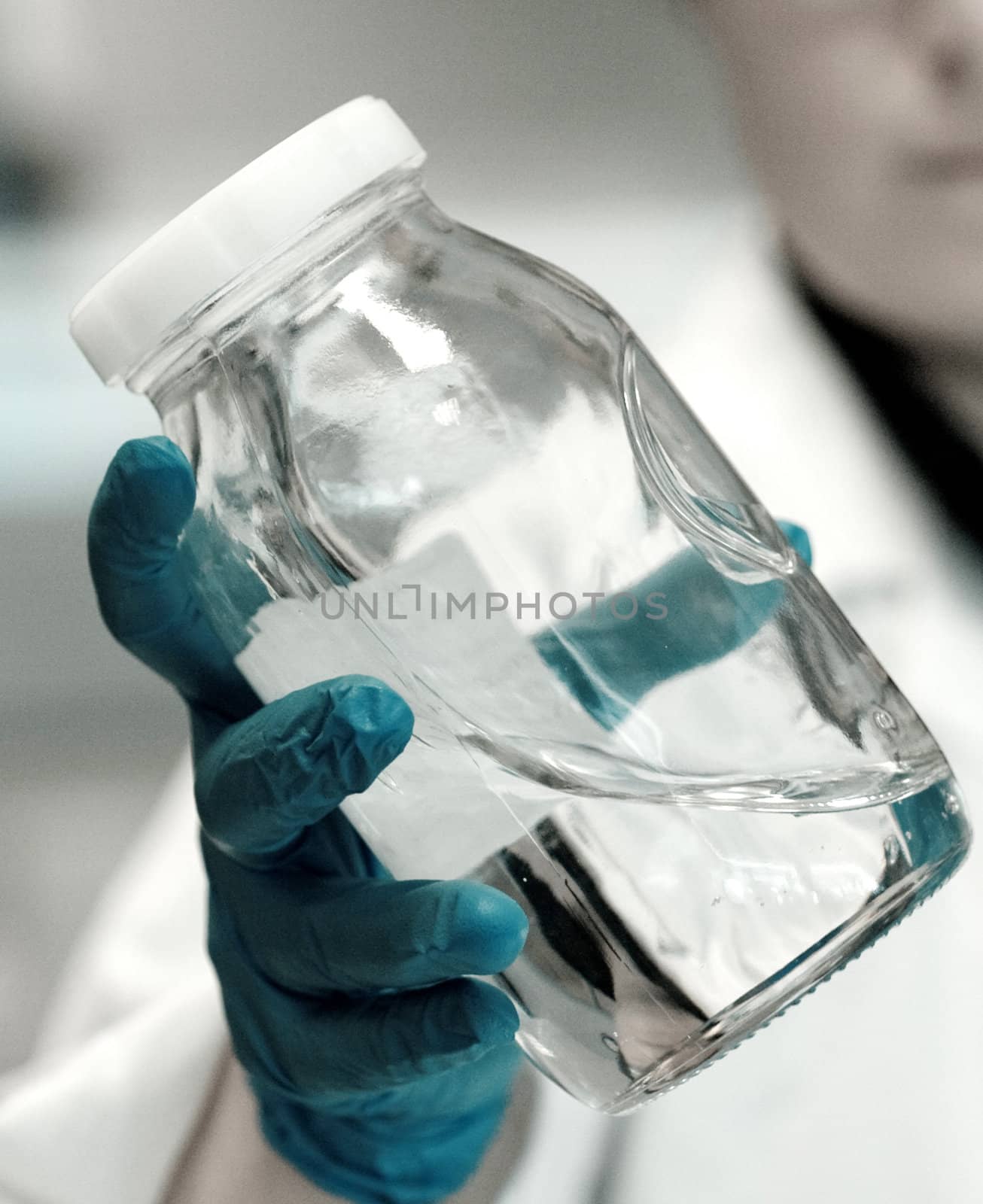 Chemist wearing blue latex gloves holding a flask full of liquid polymers in a research lab