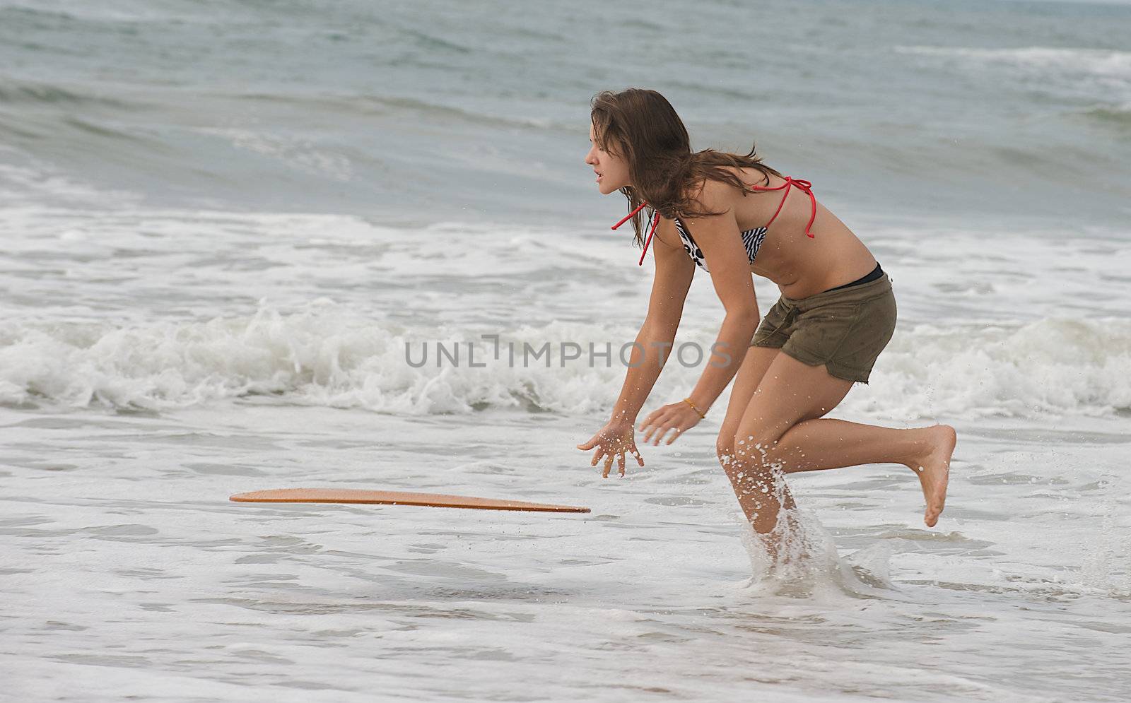 Athletic teen girl throwing skim board into surf at the beach in Emerald Isle, North Carolina.
