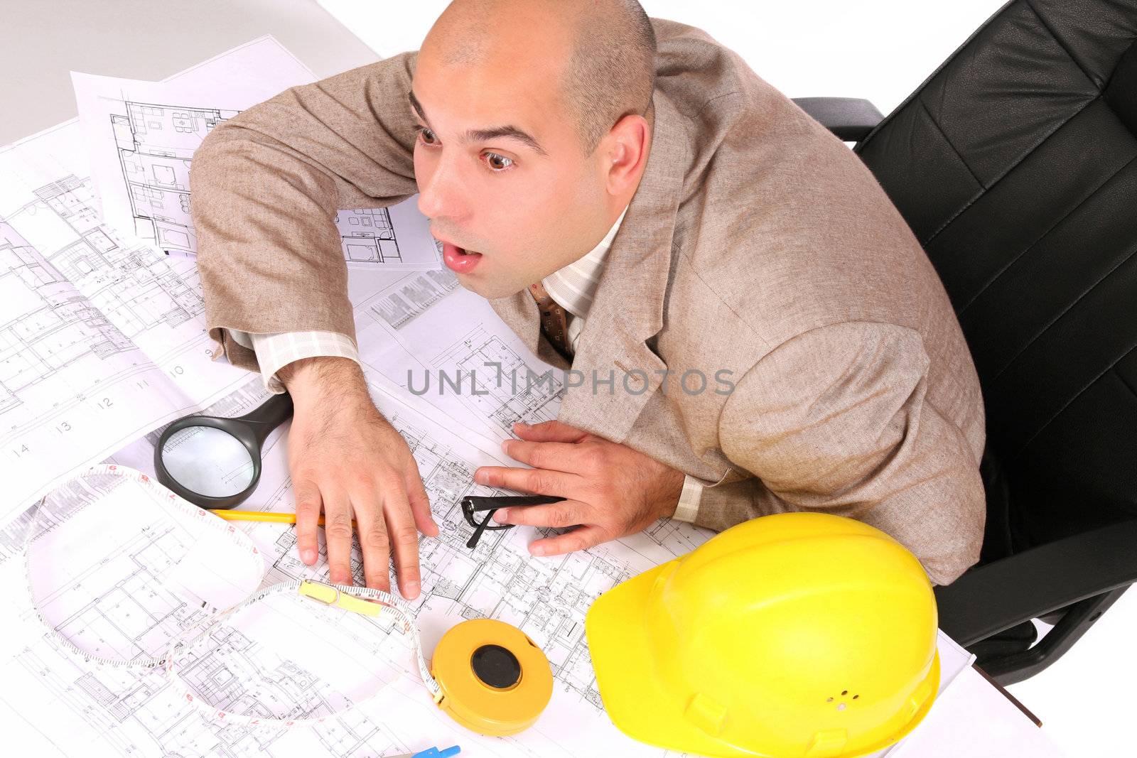 A businessman sleepy with architectural plans at desk