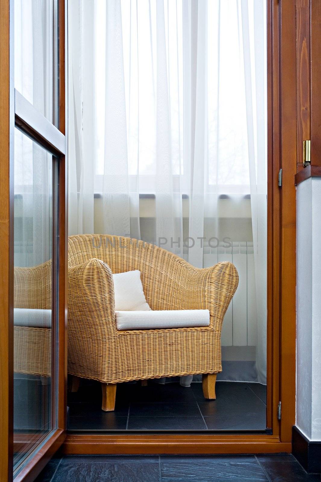Open door on a balcony on which there is a wicker chair
