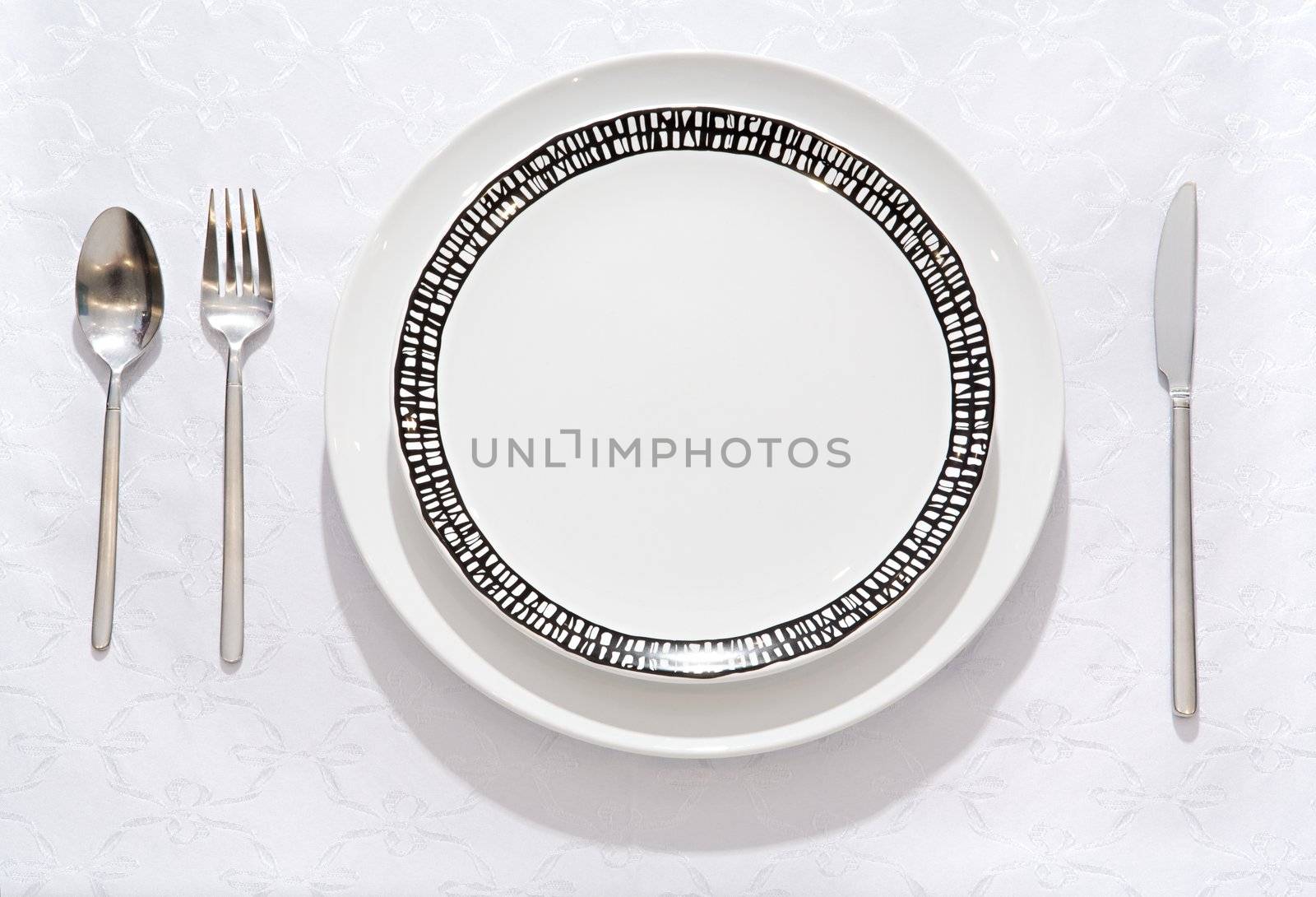 Fork, spoon, knife, empty plate on a table by Gravicapa