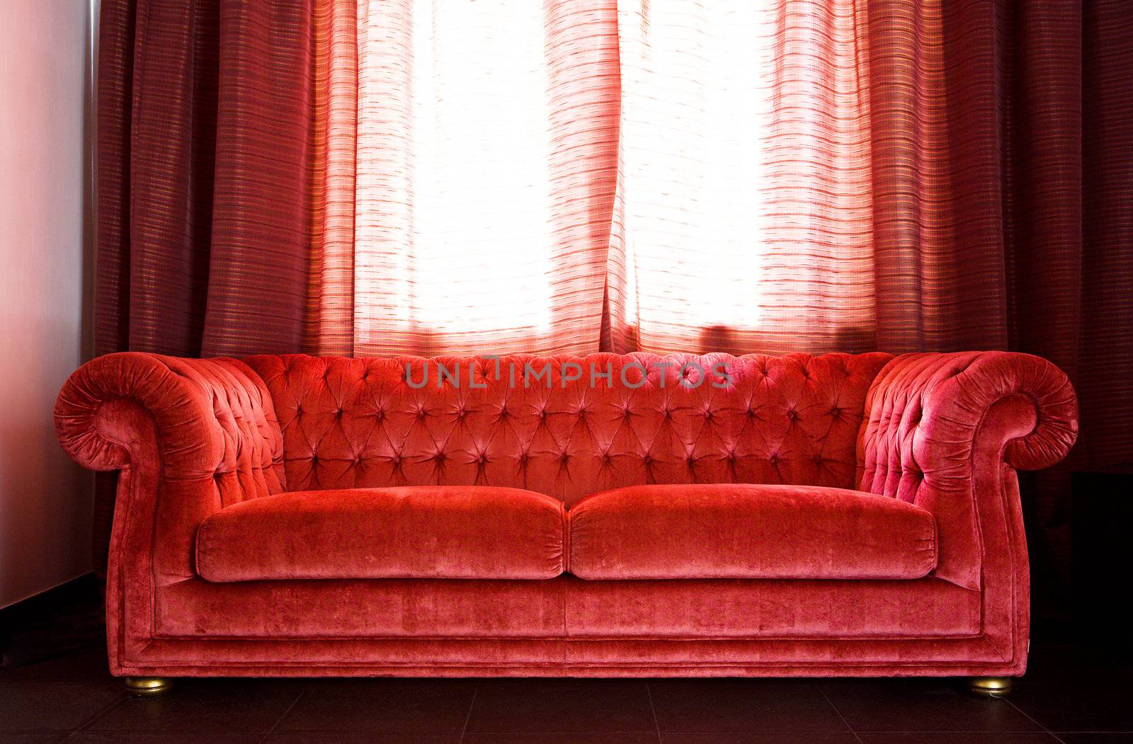 Drawing room in which there is a red sofa and a table from black marble shined with the sun through the closed curtains
