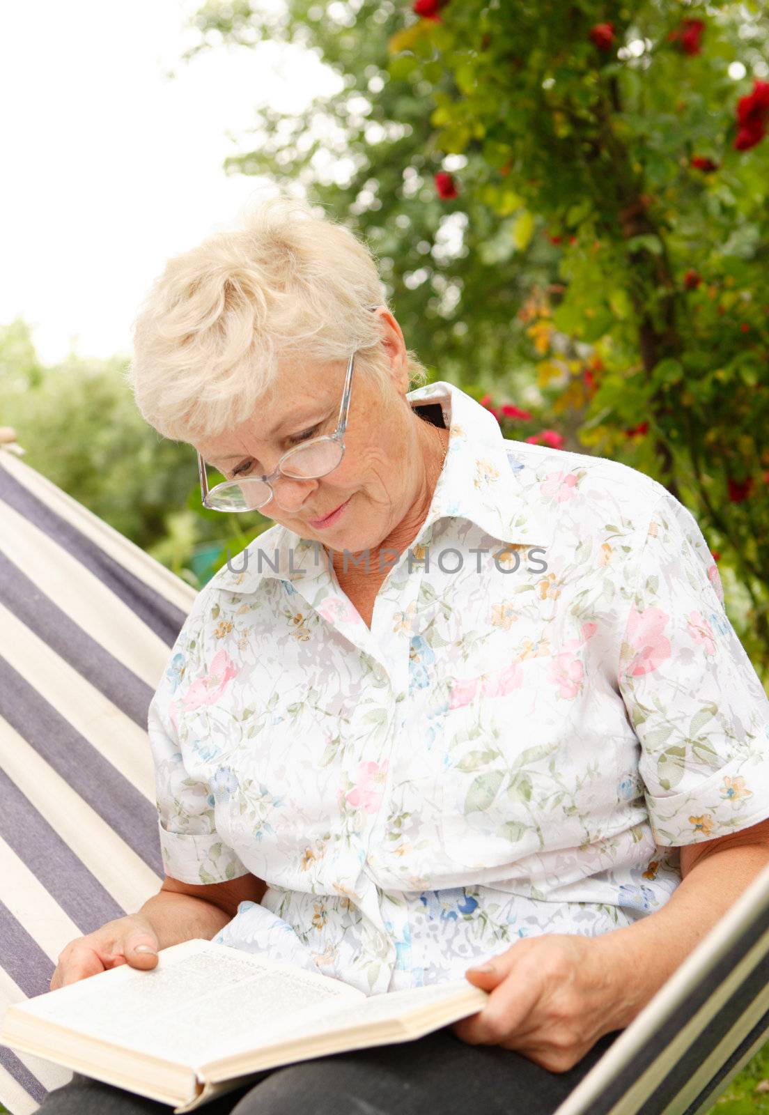 The elderly woman reads the book in a garden