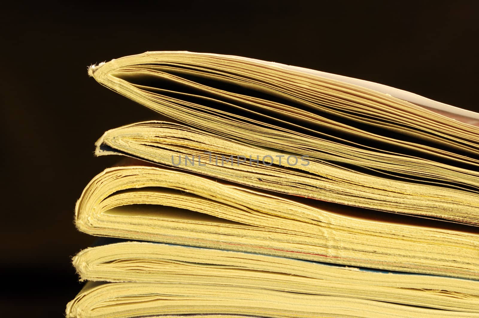 Macro of the end of a pile of oly, yellowing magazines, set against a black background, with space for text. 