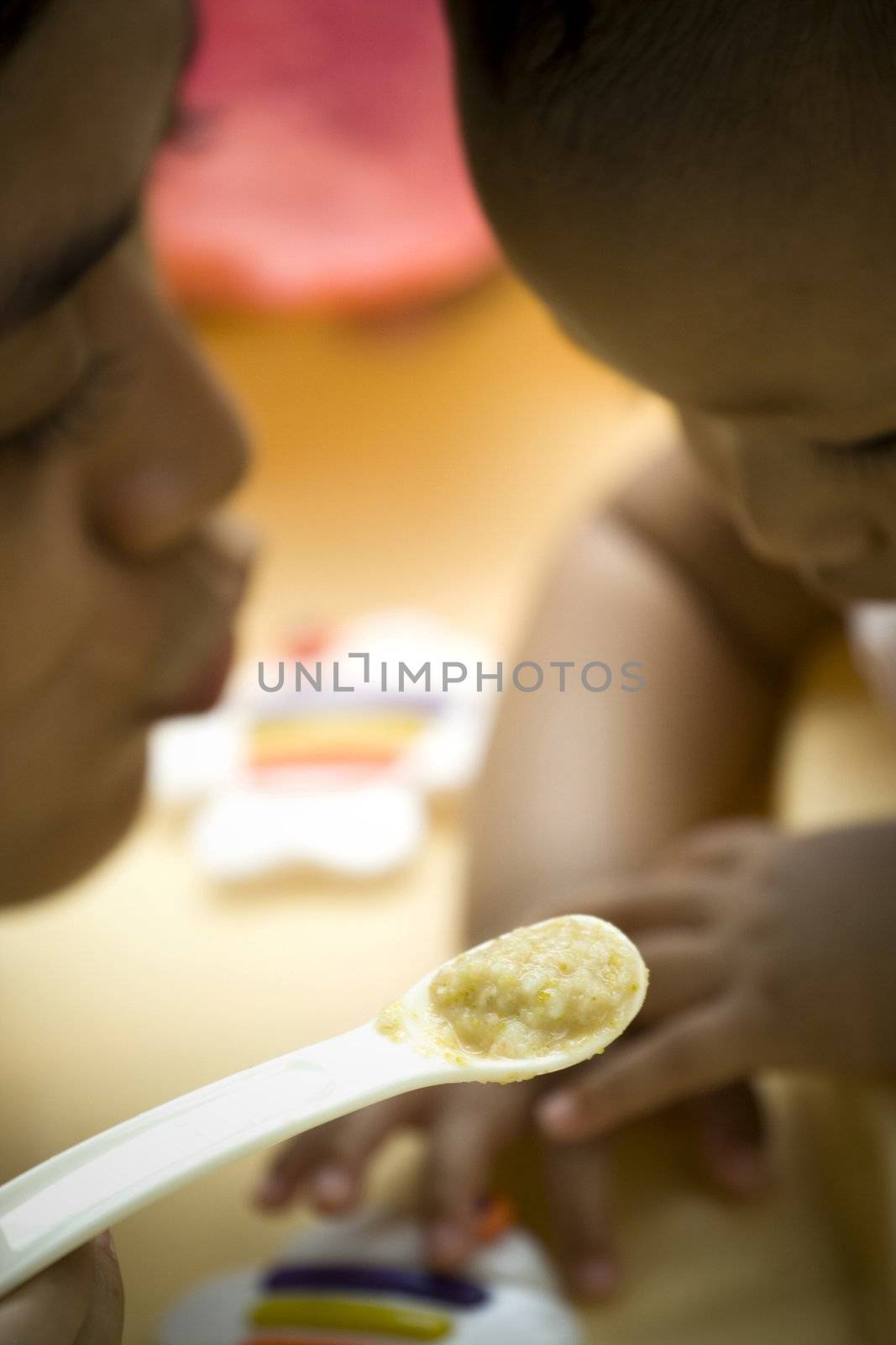 mother persuade her baby to eat during meal time. selective focused on the meal on spoon. intentionally underexposed background