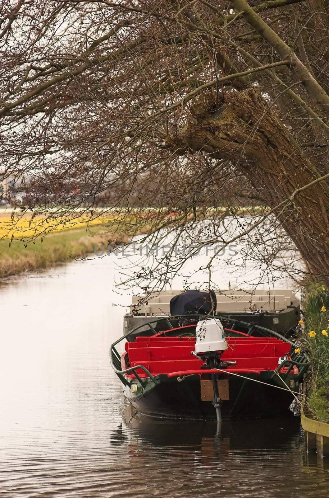 Motor boats moored at the edge of a canal next to a dutch field