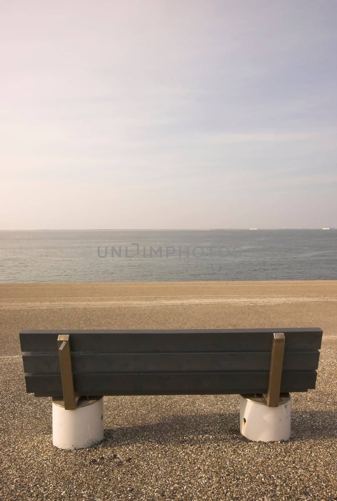 Wooden bench standing at the concrete covered seaside edge in Den Helder in Holland
