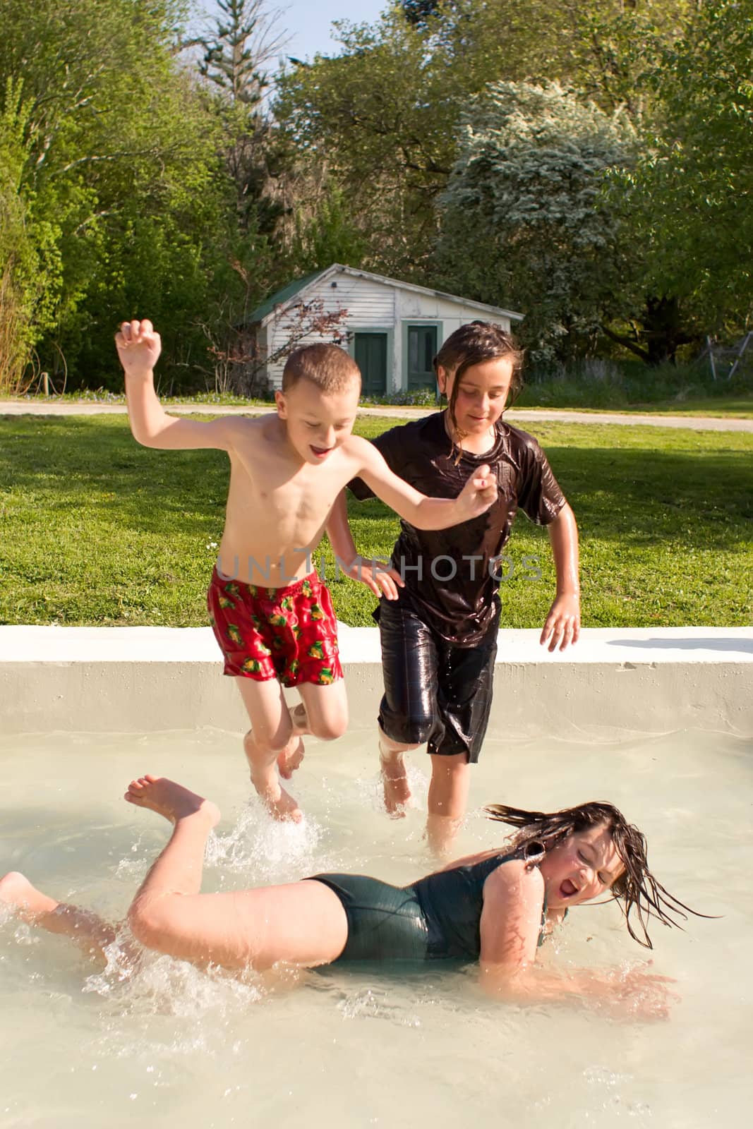 Three young people splash around in a pool on a warm spring day