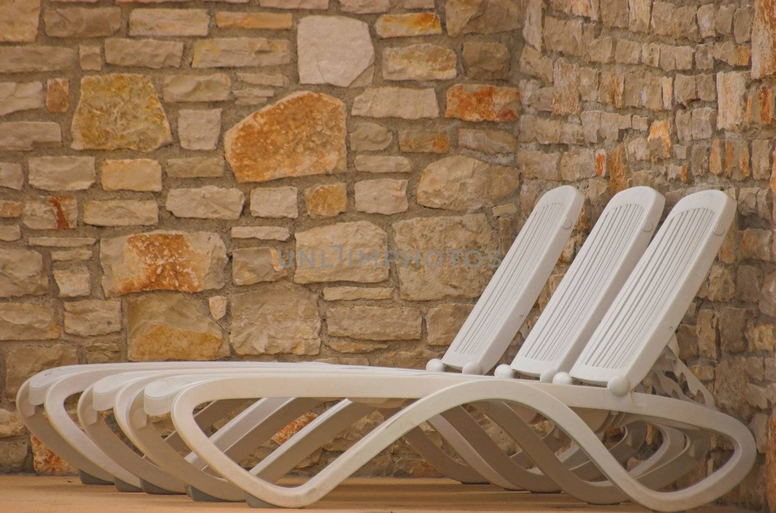 White plastic seats standing on a terrace next to a pool